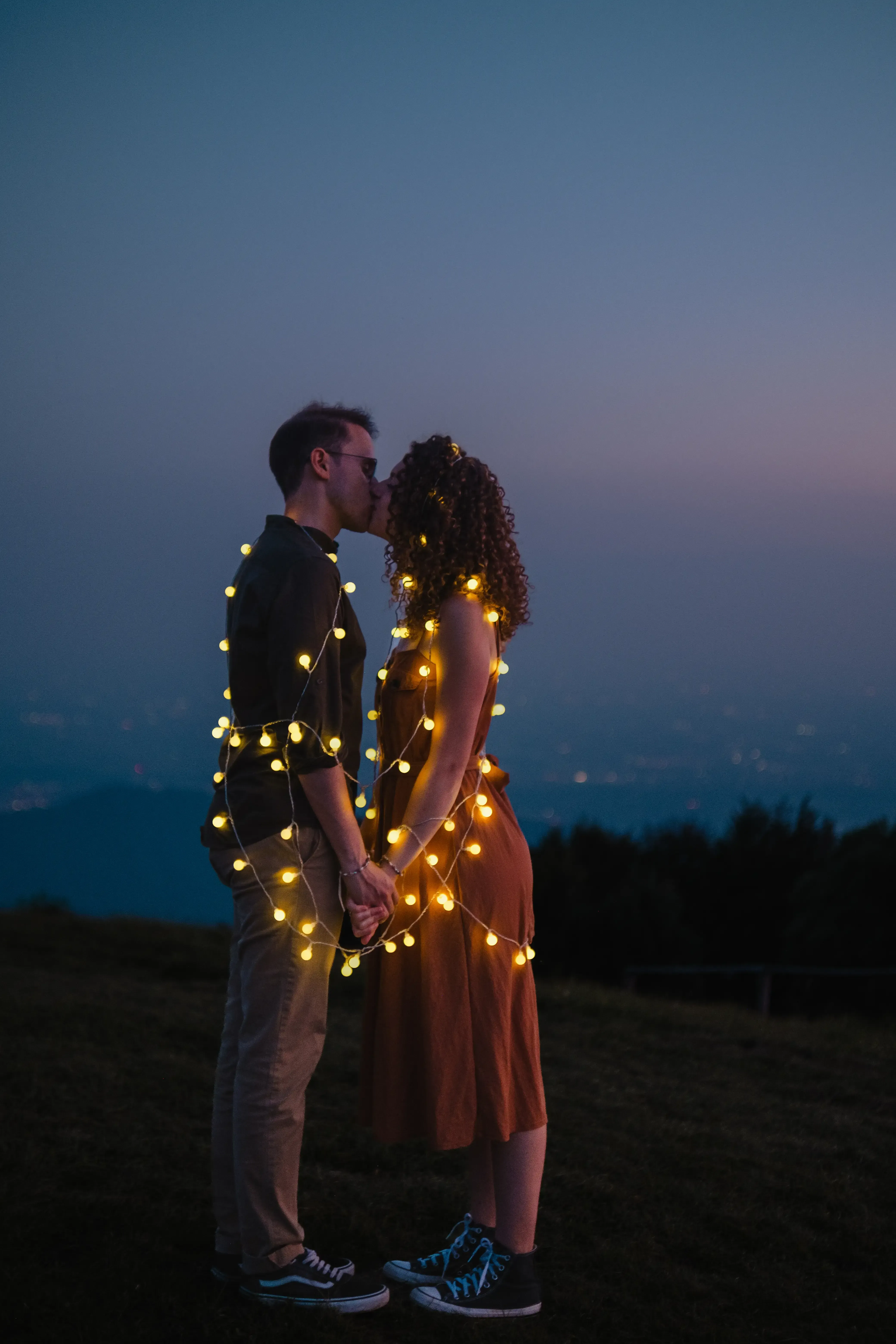 Nicolò and Greta hugging, illuminated by small string lights draped over them.