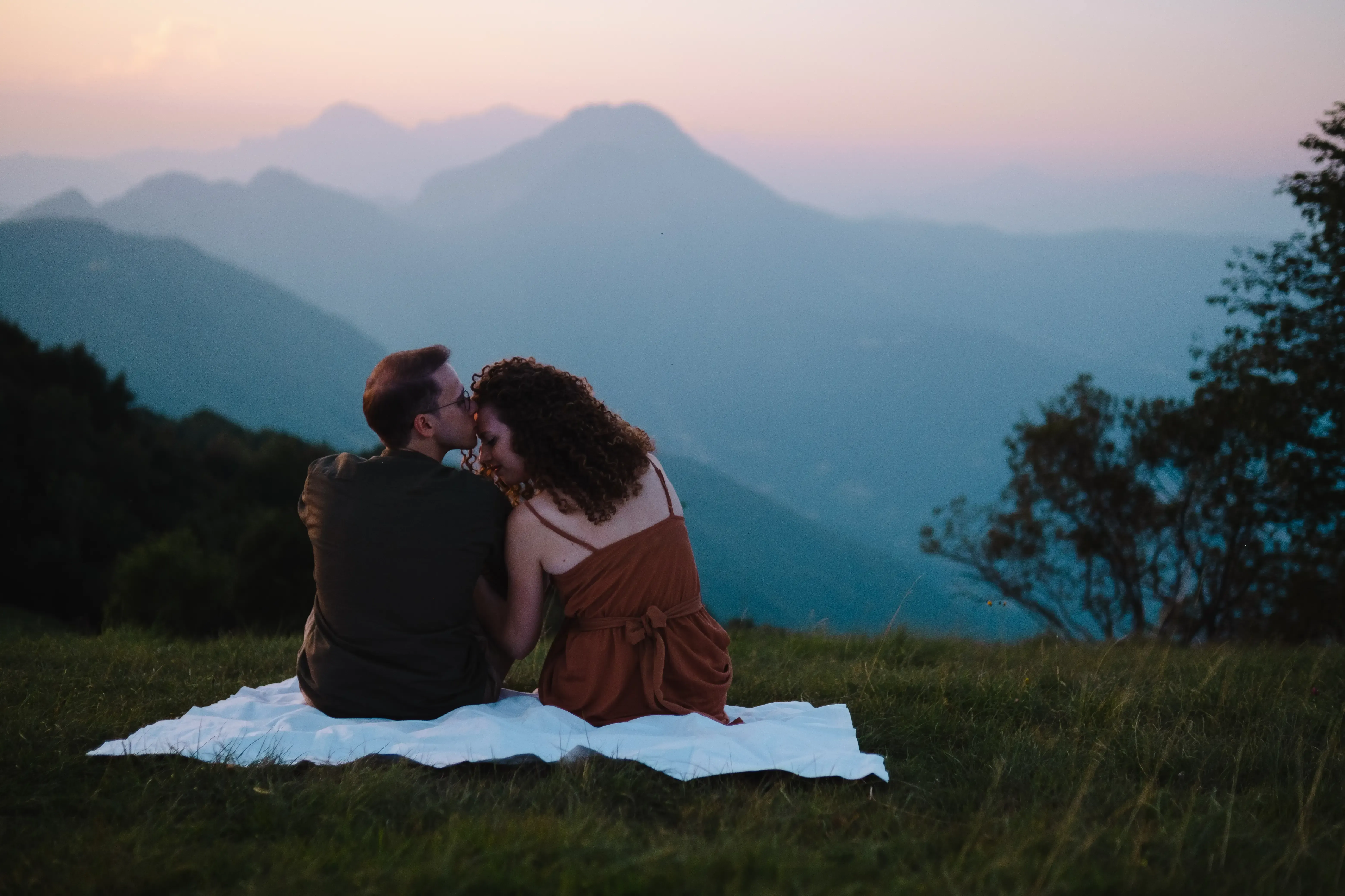 Nicolò kissing Greta's forehead while sitting on a picnic blanket.