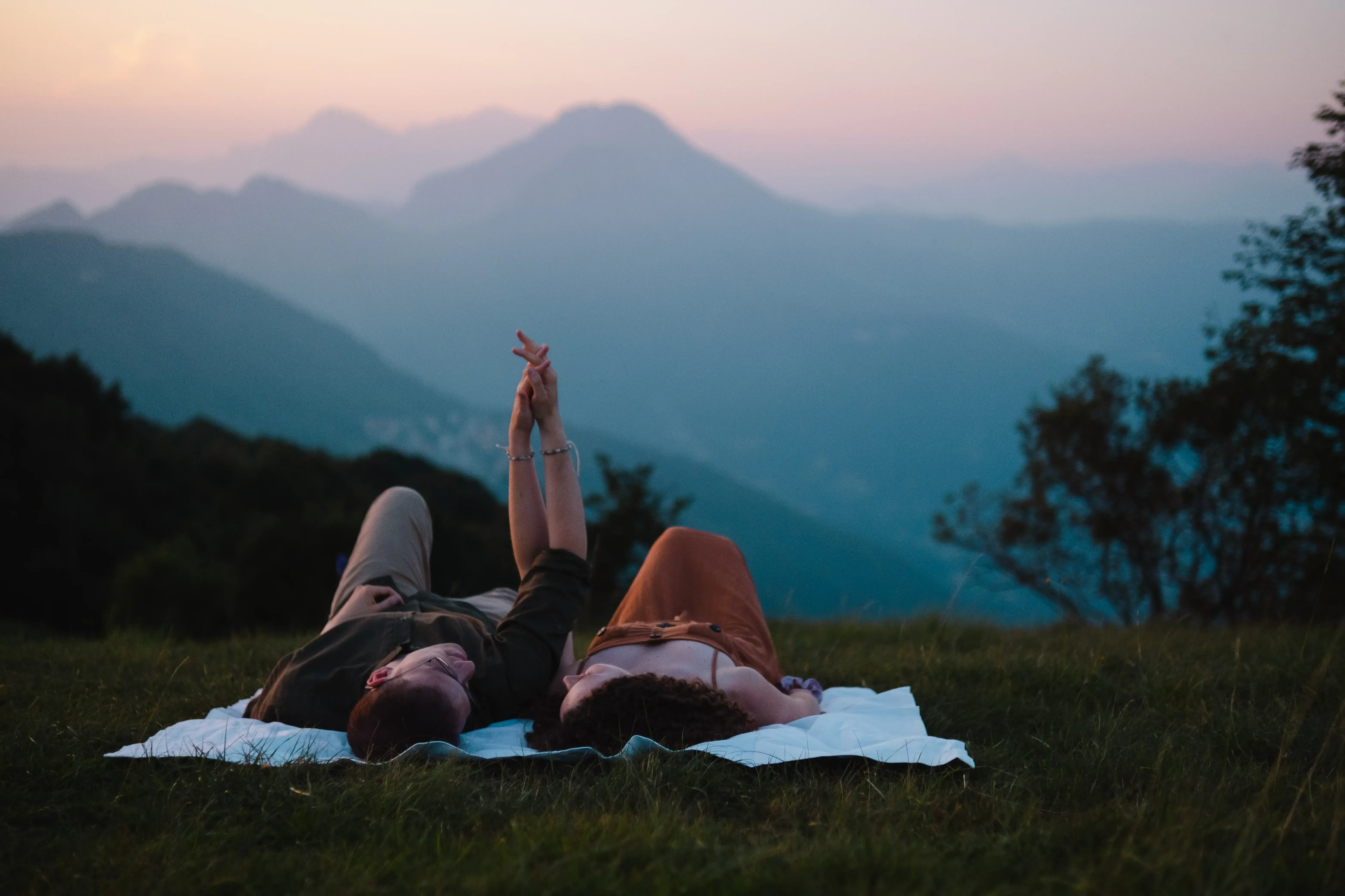 Nicolò and Greta lying on the ground, holding hands gently.