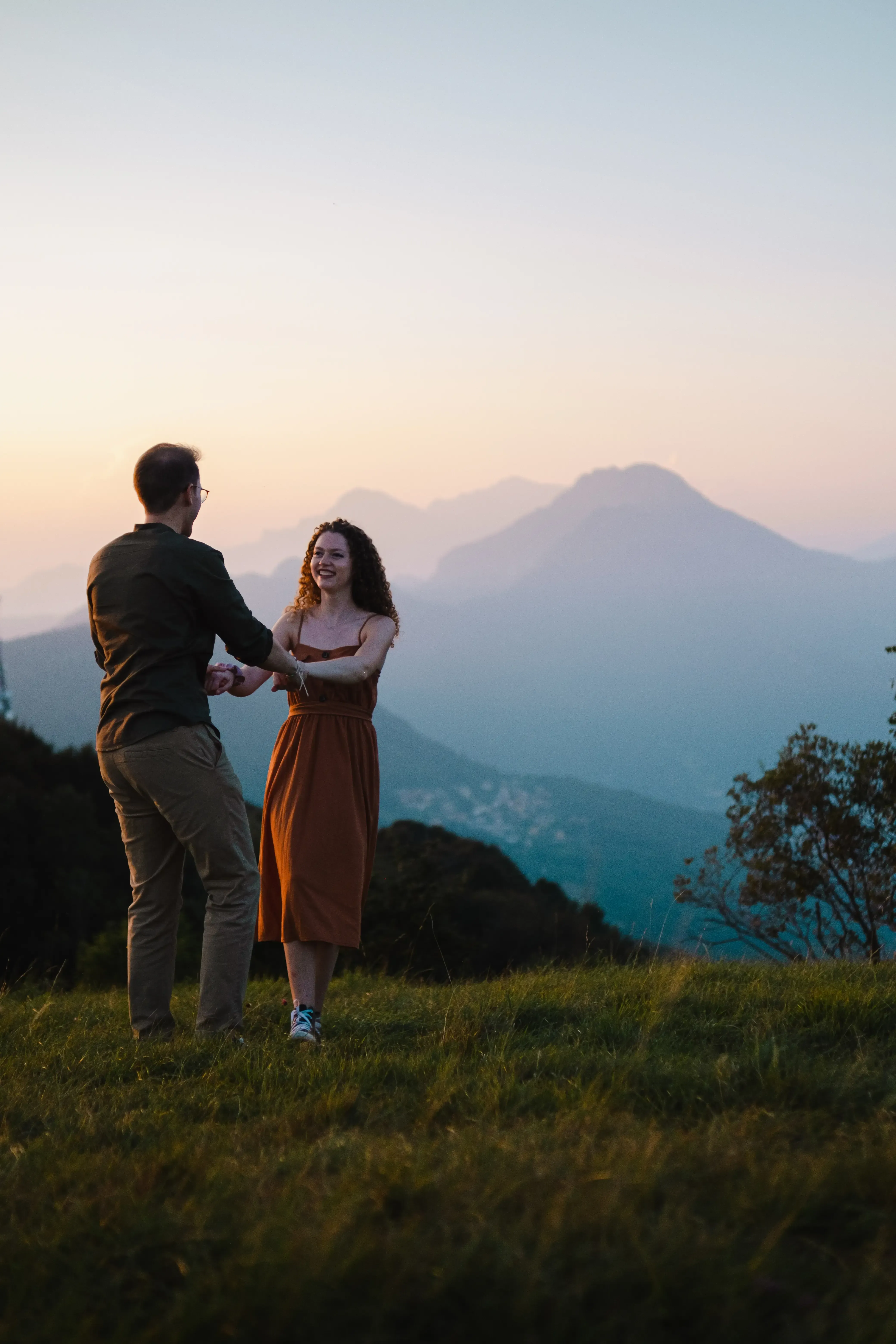 Nicolò and Greta dancing joyfully in the grass on a mountain peak.