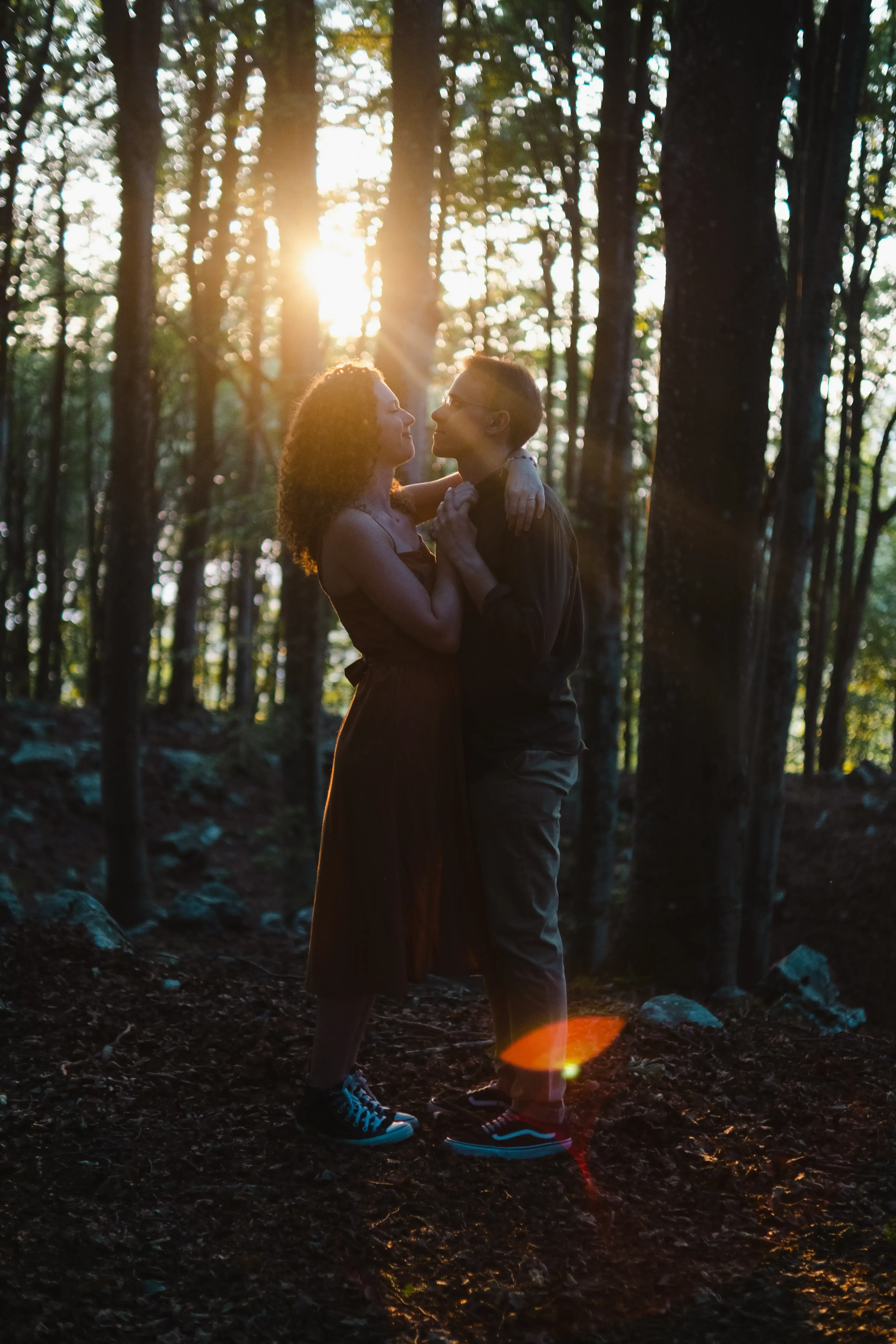 Nicolò and Greta hugging in the forest with sunlight flaring behind them.