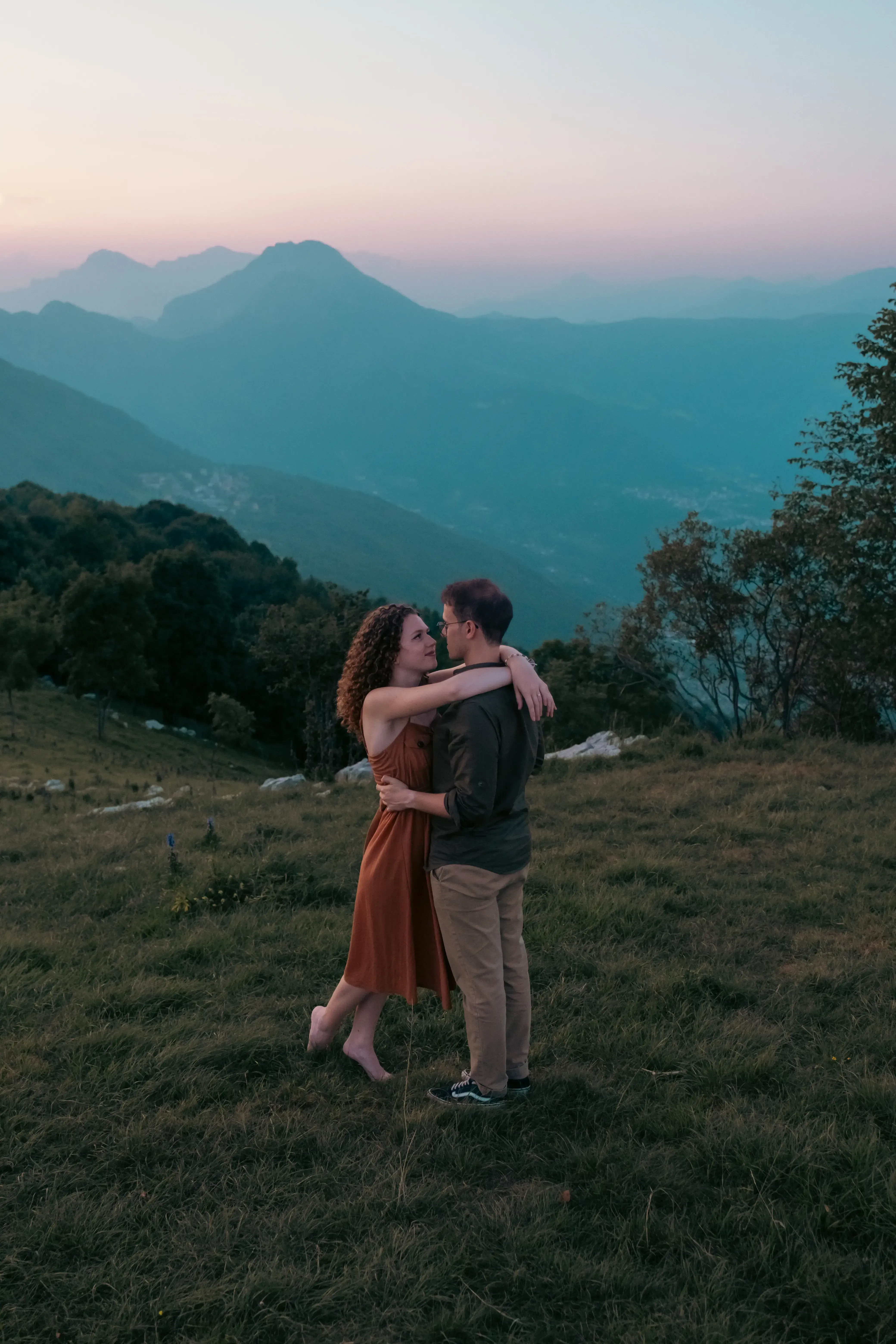 The couple embracing warmly in the center of the scenic mountain meadow.