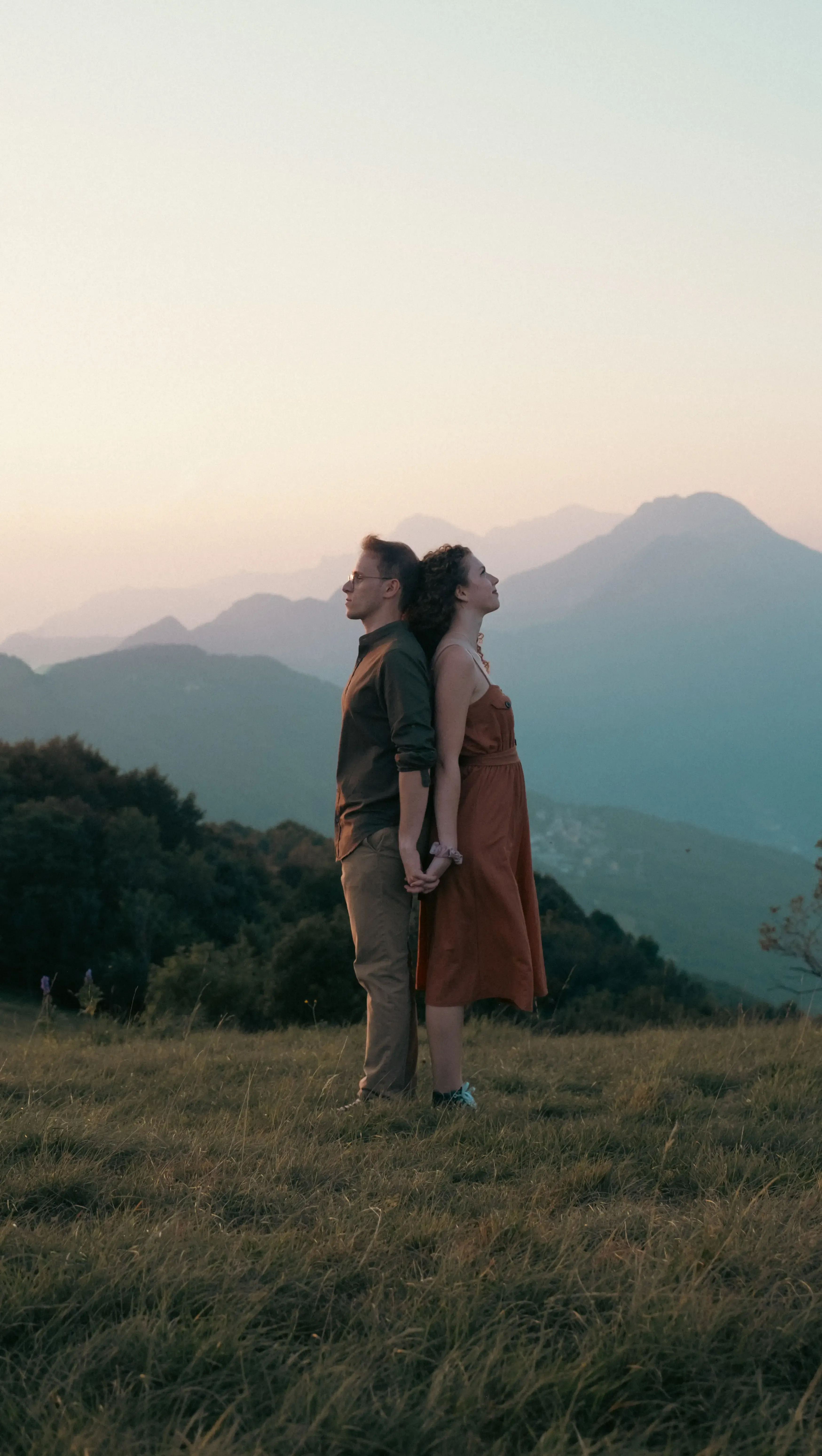 Nicolò and Greta standing back to back in a scenic mountain meadow.