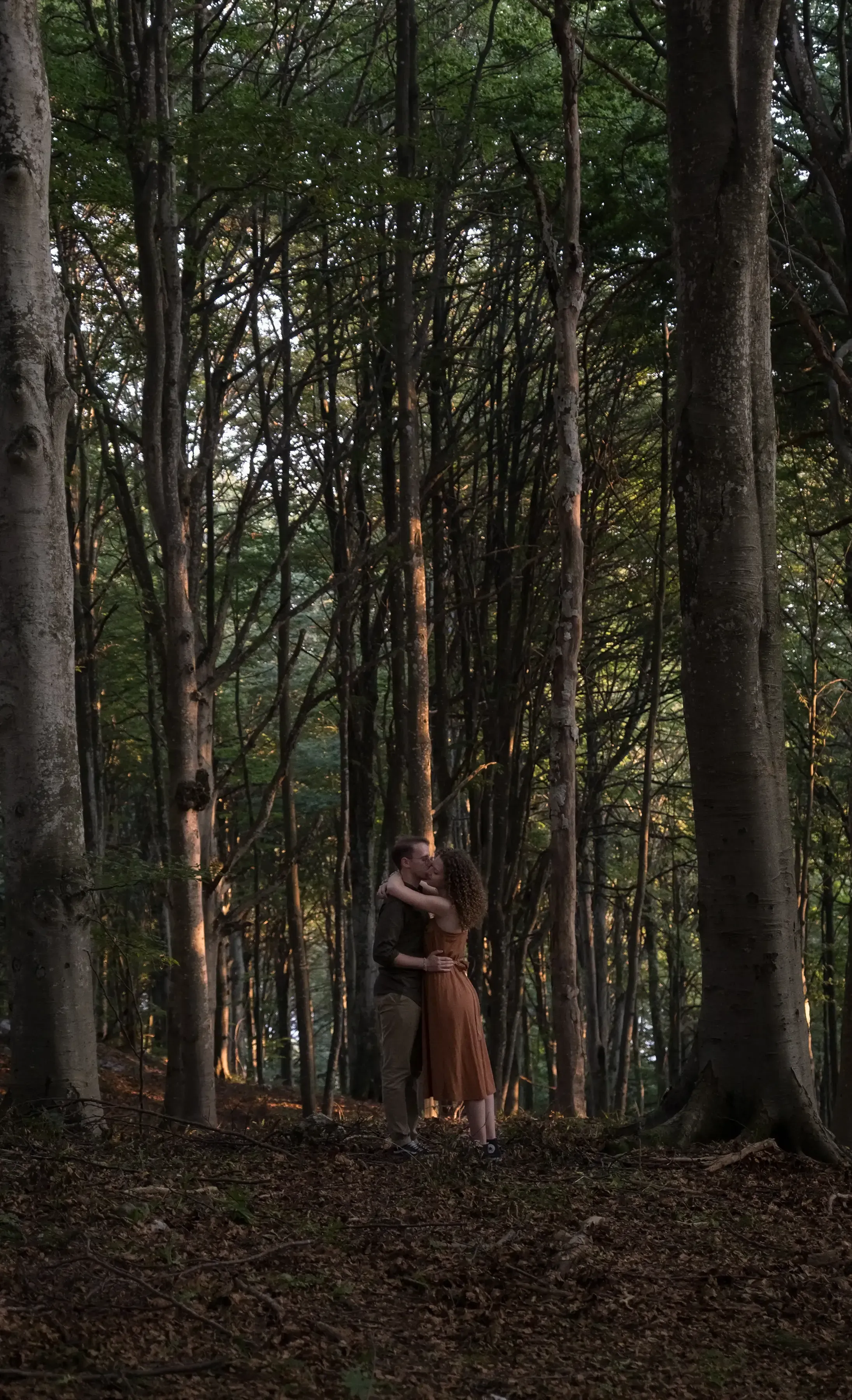 Nicolò and Greta embracing deeply in a sun-dappled forest on Mount Linzone.