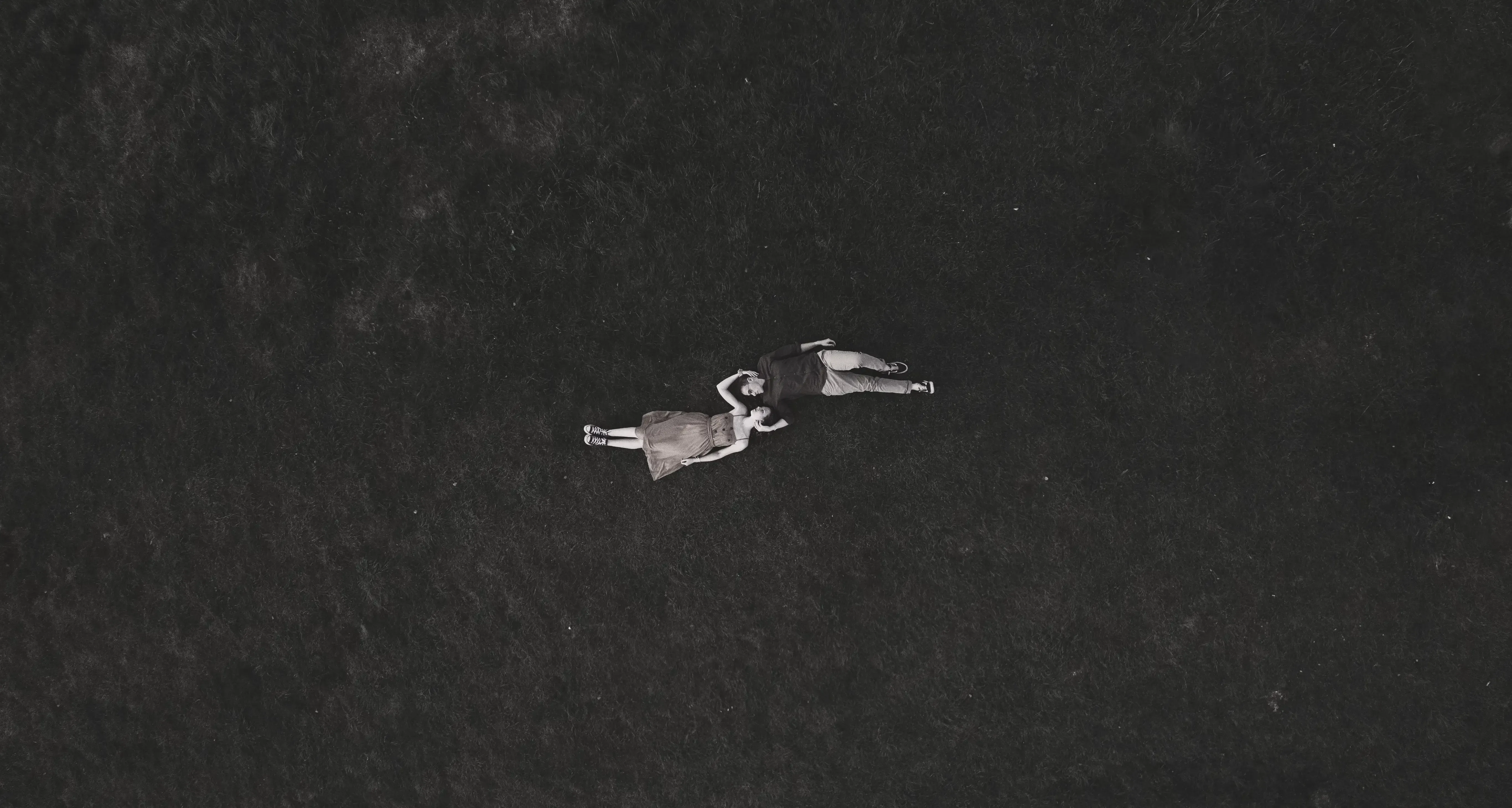 Aerial drone shot of Nicolò and Greta lying close together in the mountain meadow.