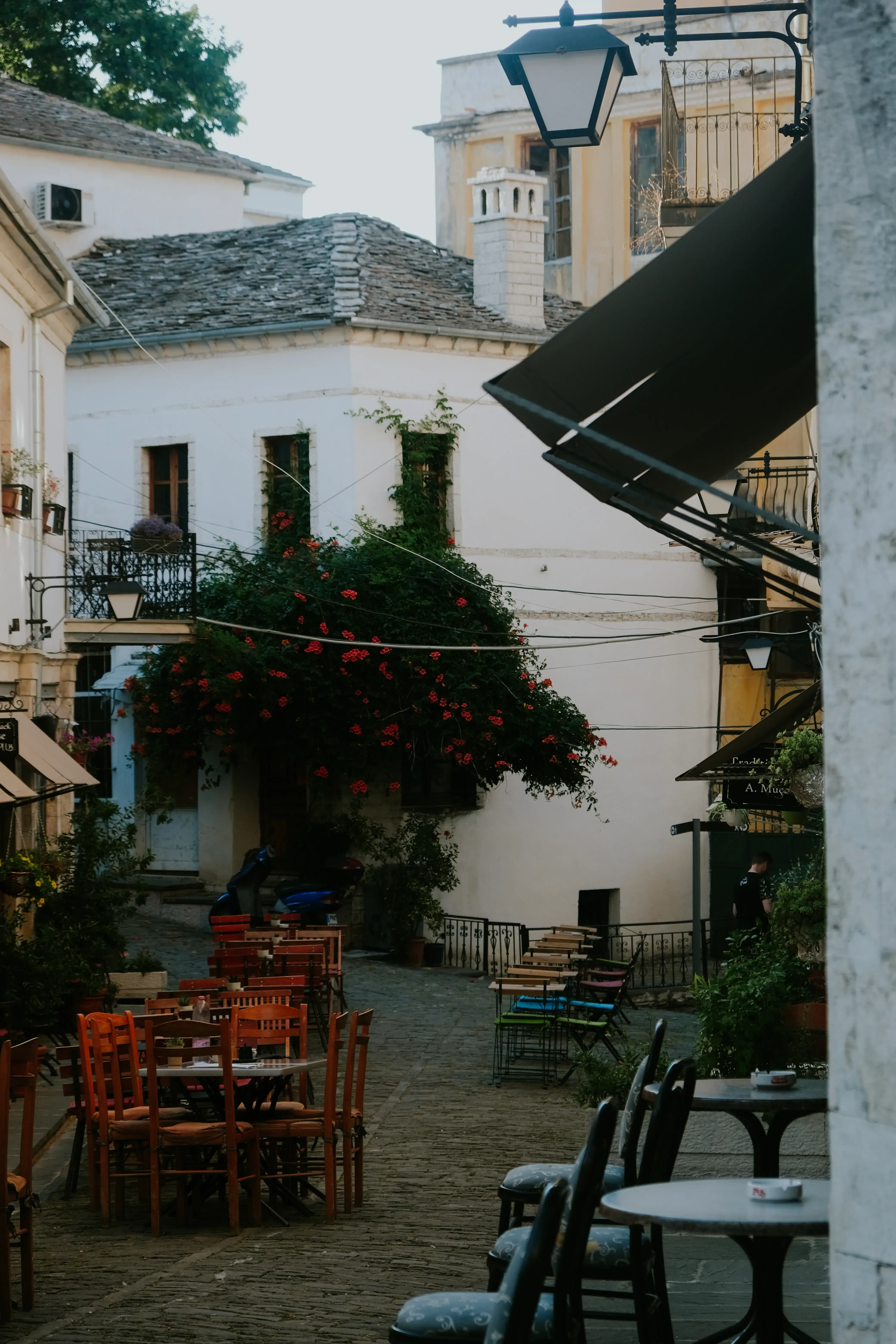 A charming, characteristic Berat street scene featuring cafe tables set out under the historic stone houses.