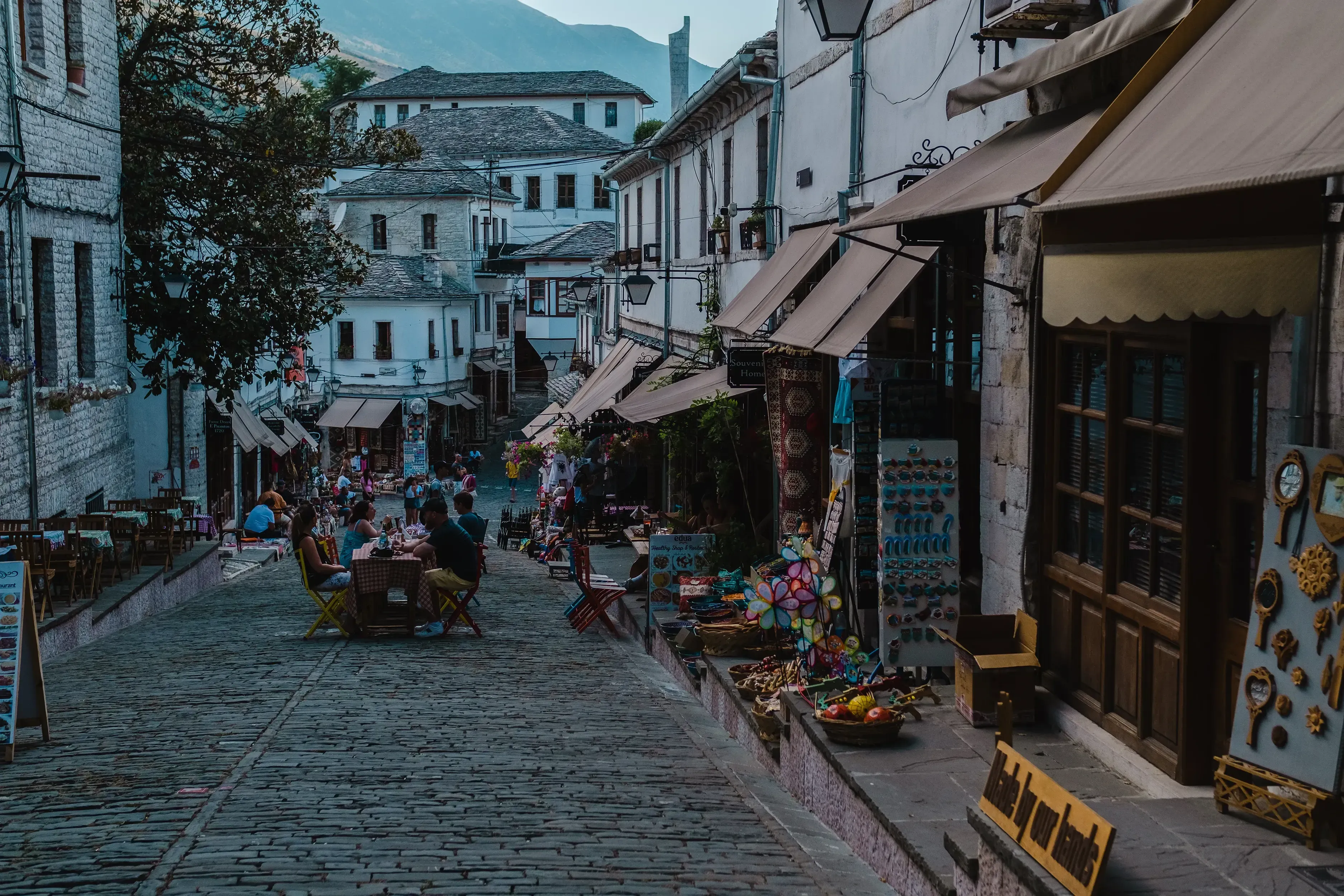 A charming, characteristic Berat street scene featuring cafe tables set out under the historic stone houses.