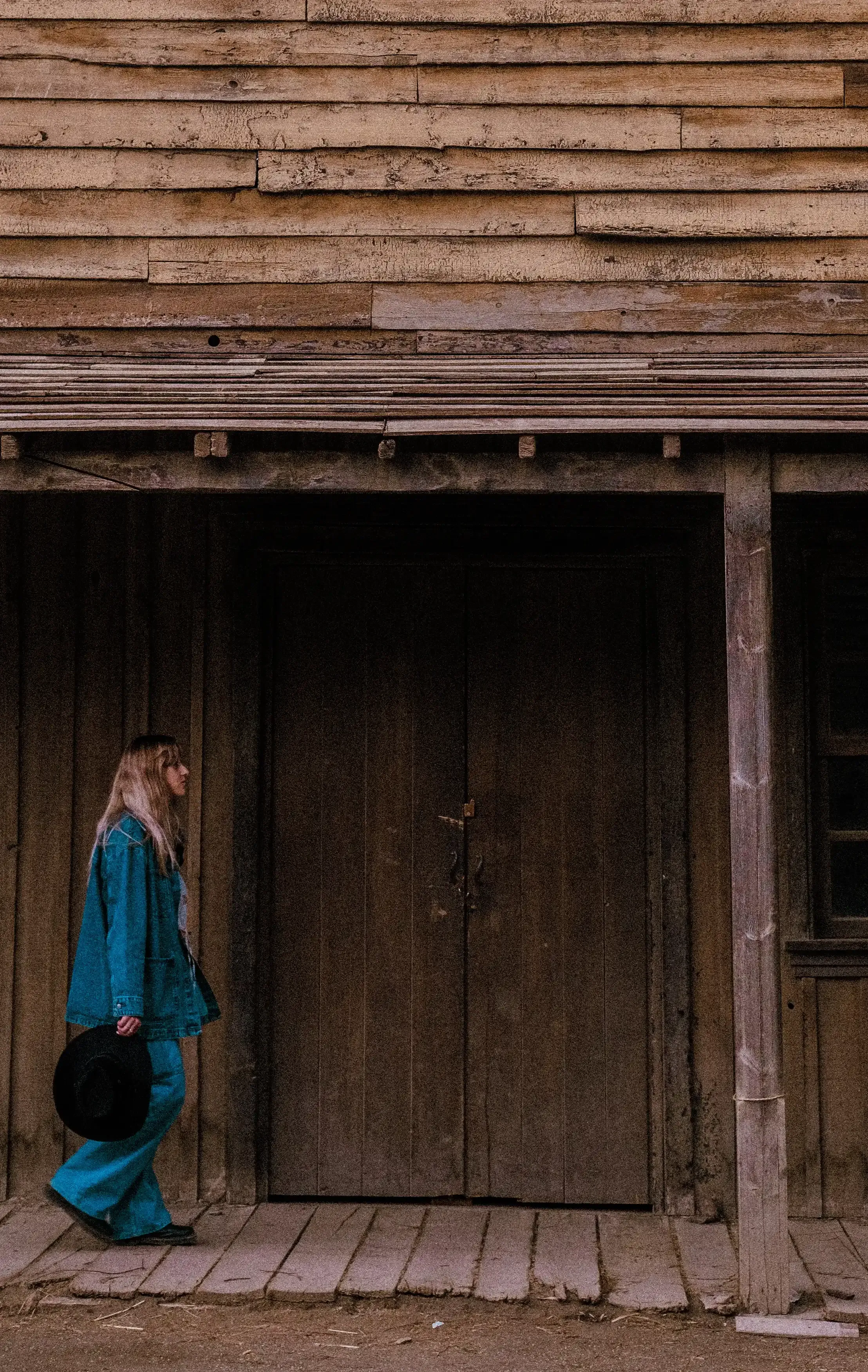 Letizia walking past a wooden house in the Fort Bravo set.
