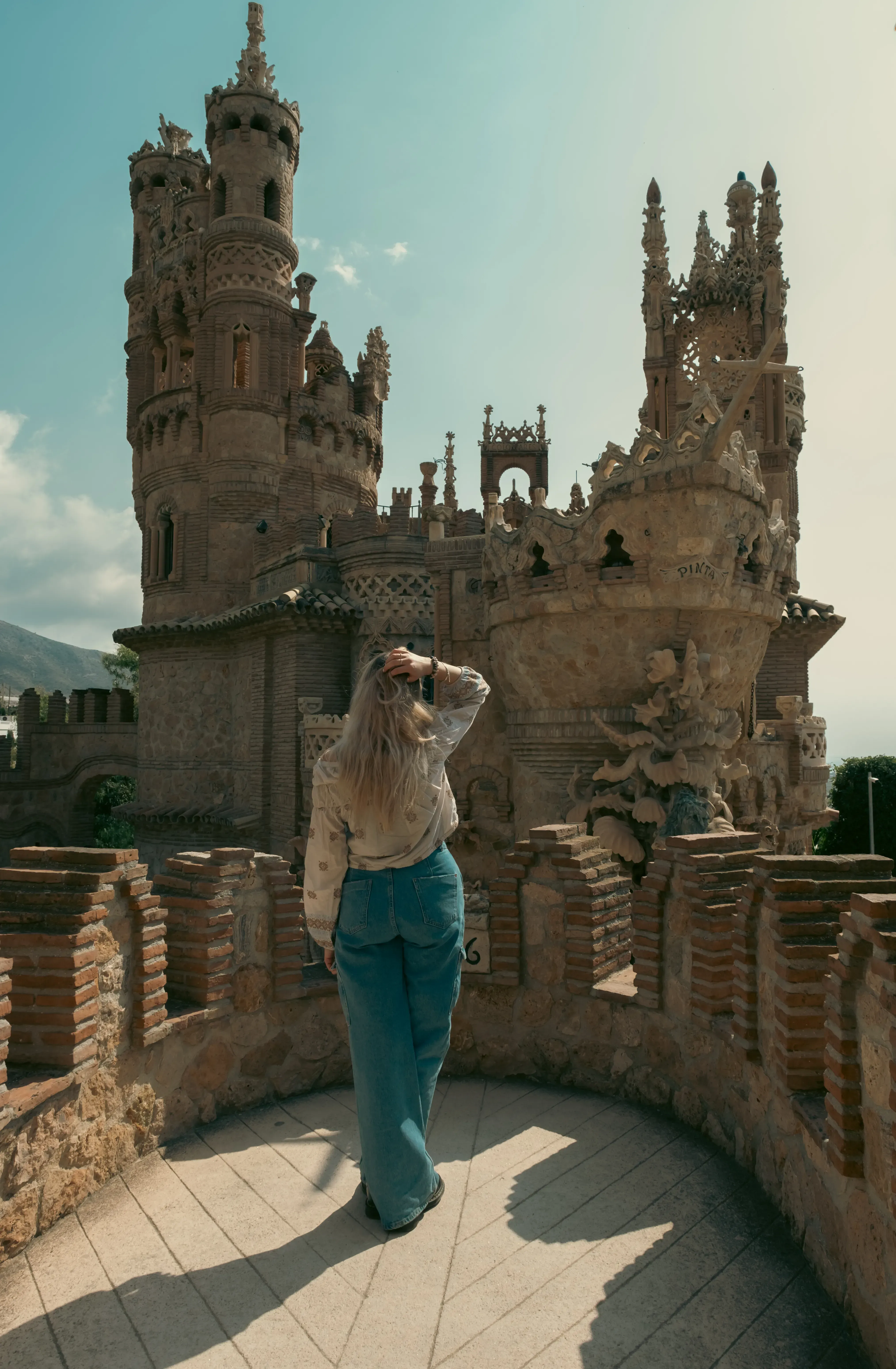 Letizia standing at the top of Castillo de Colomares, viewed from behind, looking out over the landscape.