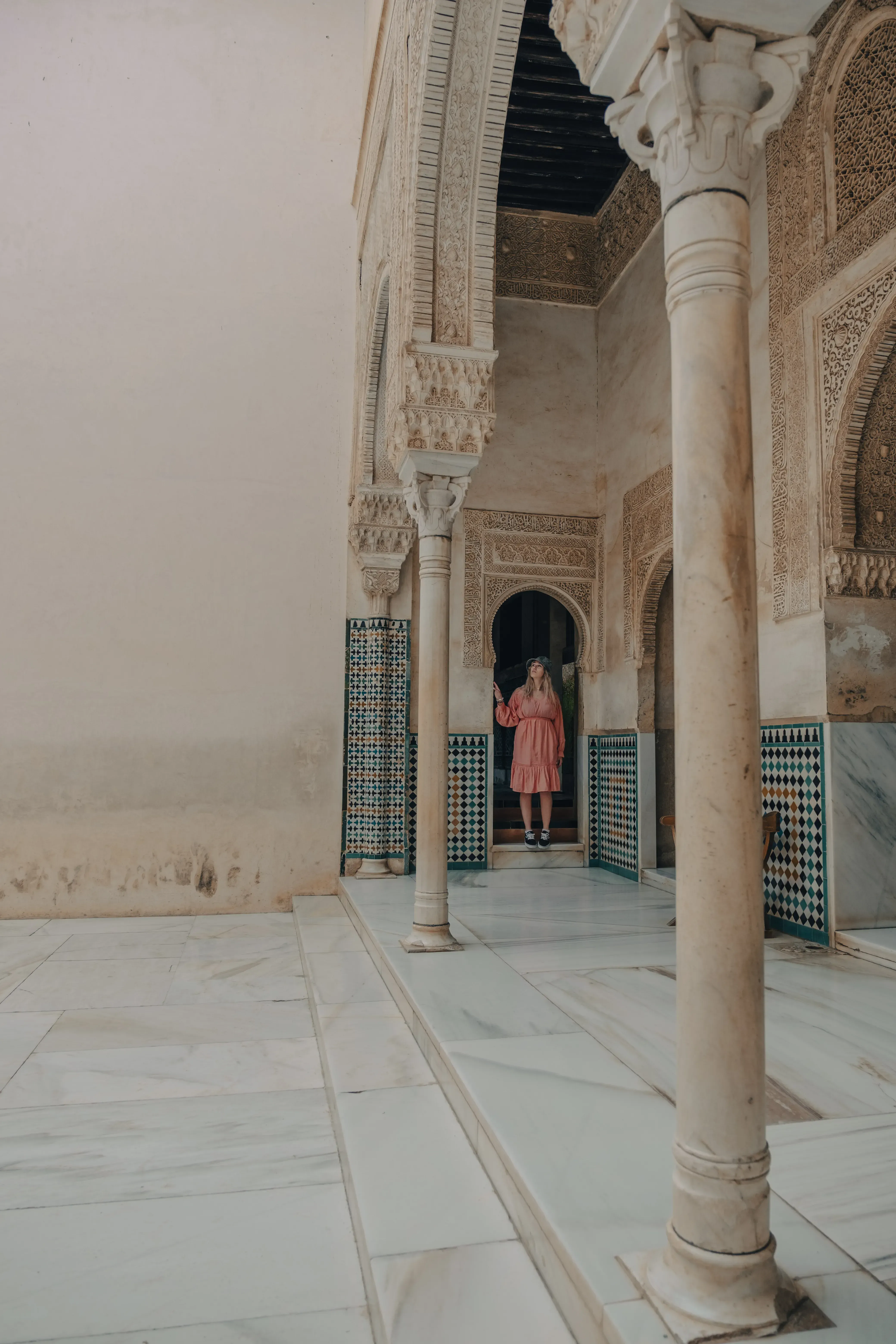 Letizia stepping out of a carved wooden doorway, transitioning from the interior of the Alcázar to the serene gardens.