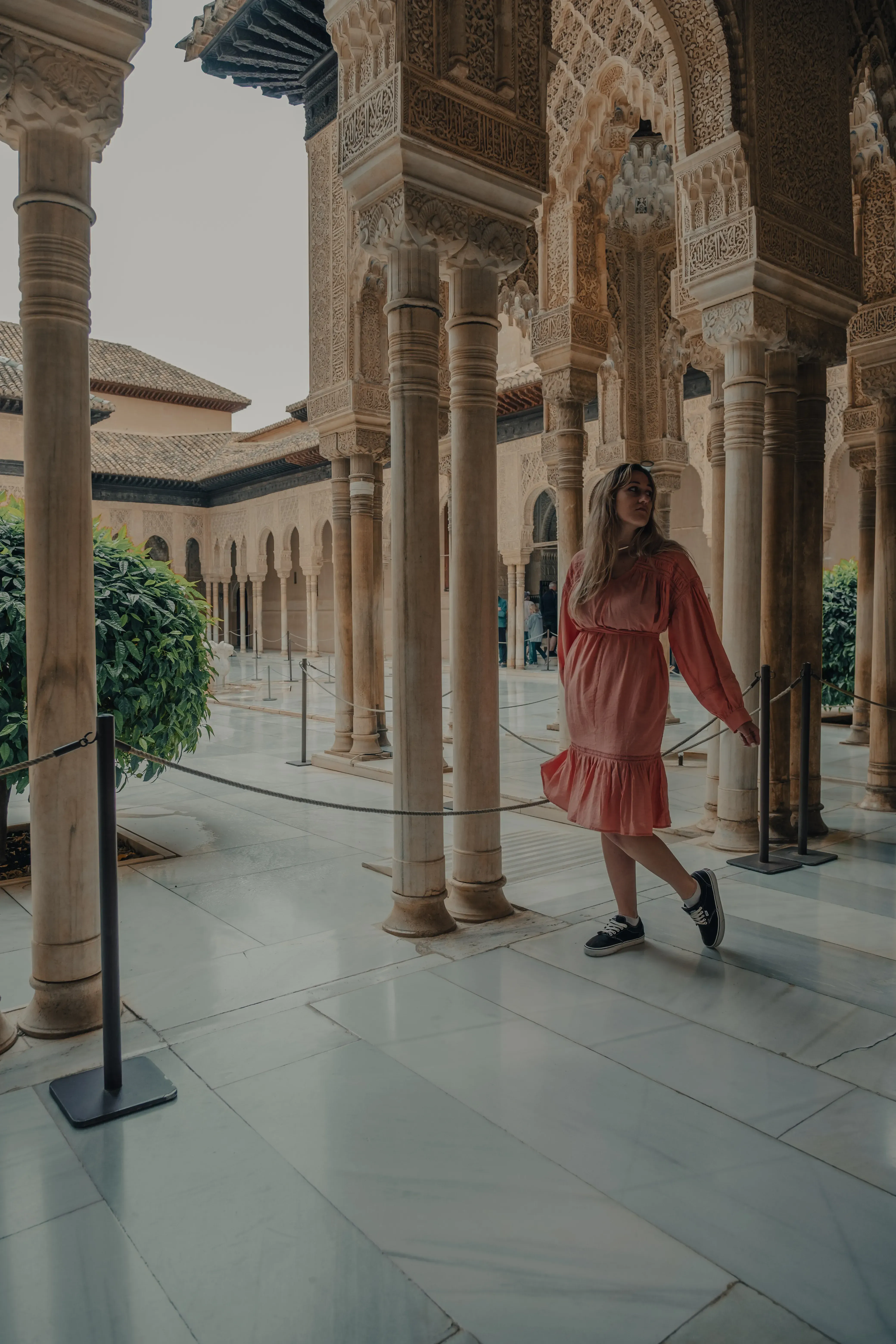 Letizia standing near a decorative horseshoe arch inside the courtyards of the Royal Alcázar palace in Seville.