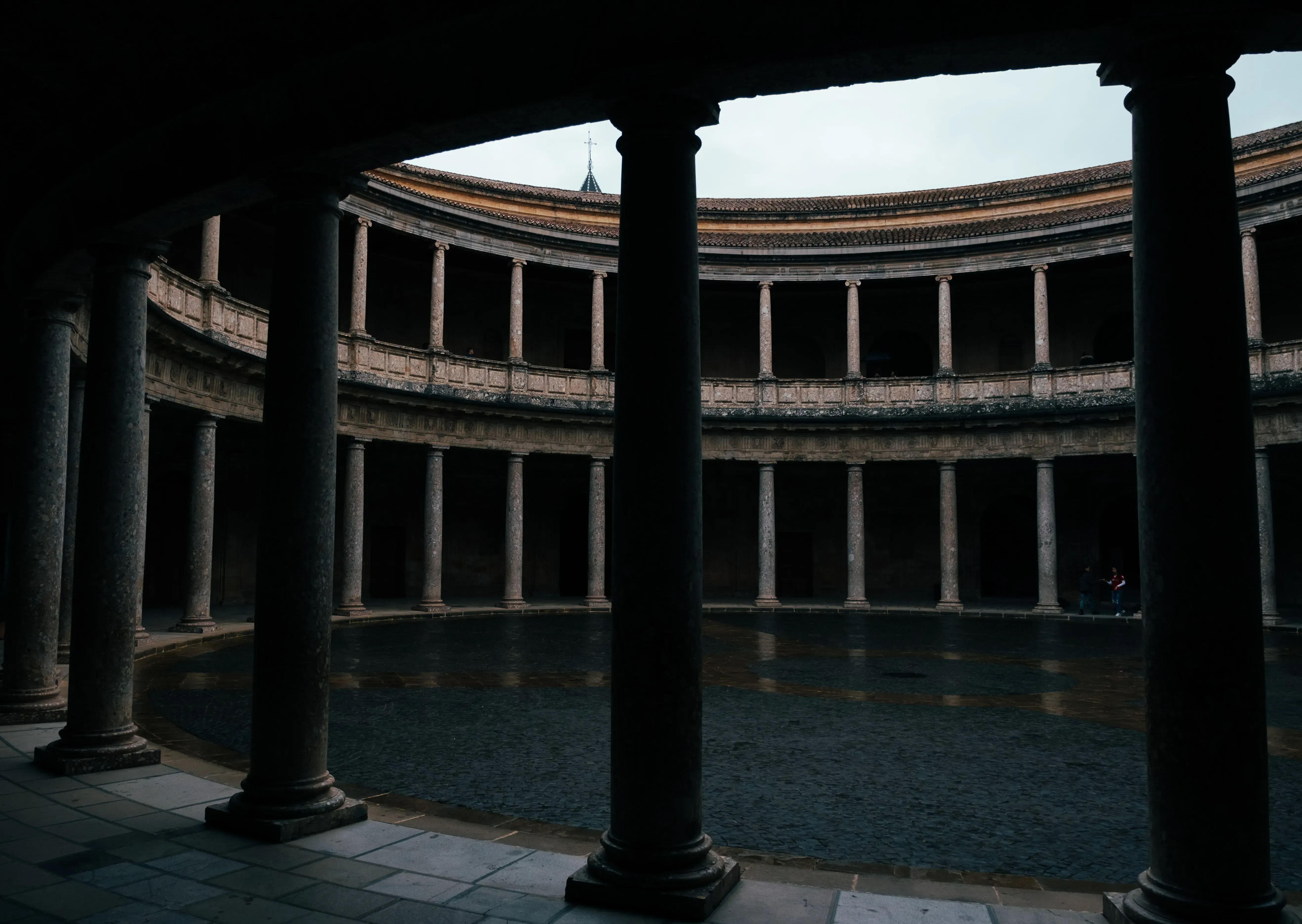 An ancient, tiered, oval ruin structure resembling the Roman Colosseum (e.g., the Roman Amphitheater ruins in Spain).