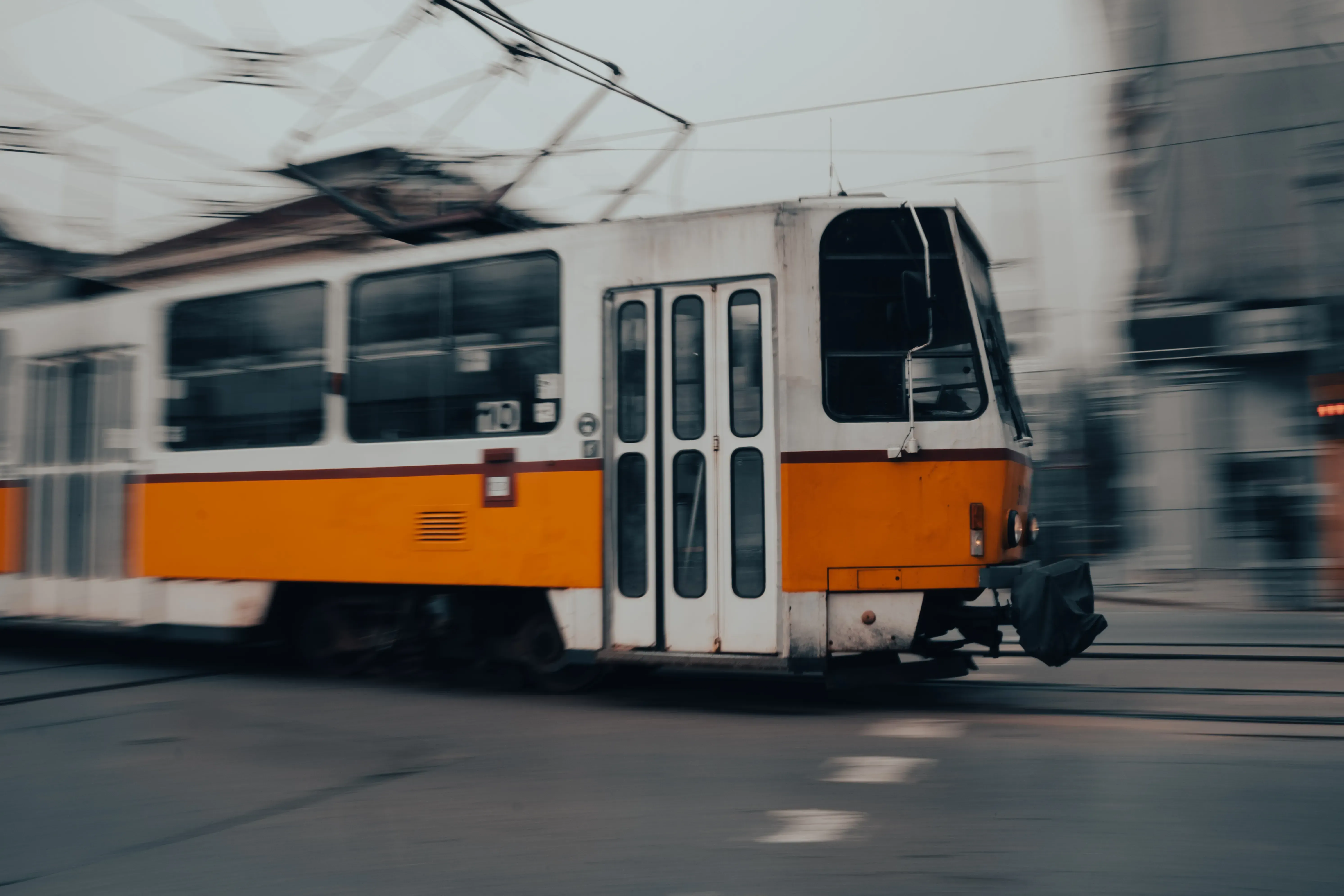 An orange public tram speeding along the tracks in the city of Sofia.