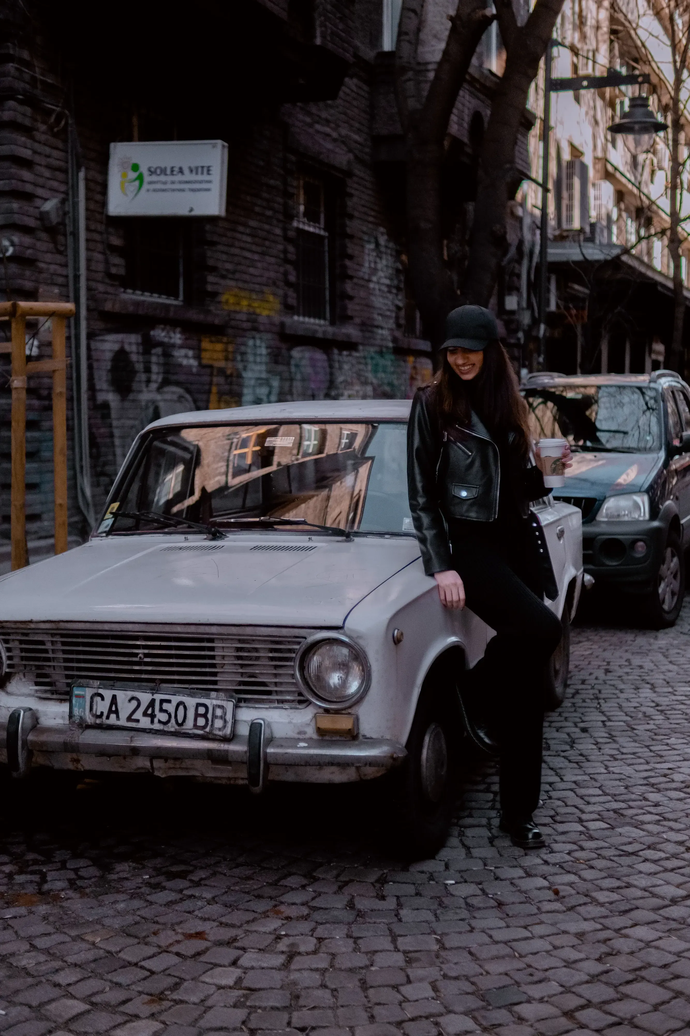 A vintage car parked or driving on the streets of Sofia with Miriam next to it.