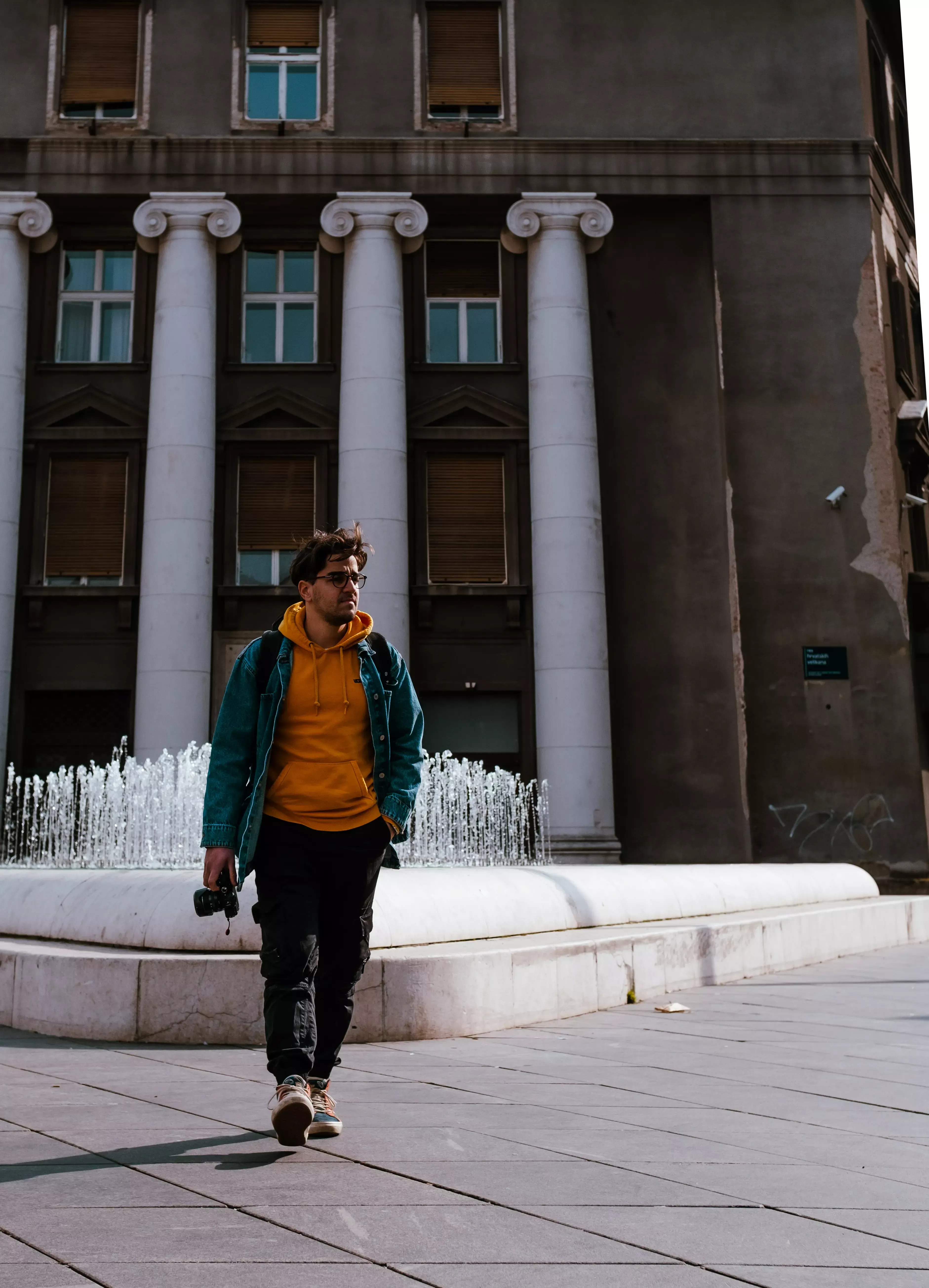 Ieser walking past a large, elaborate stone fountain in a city square.