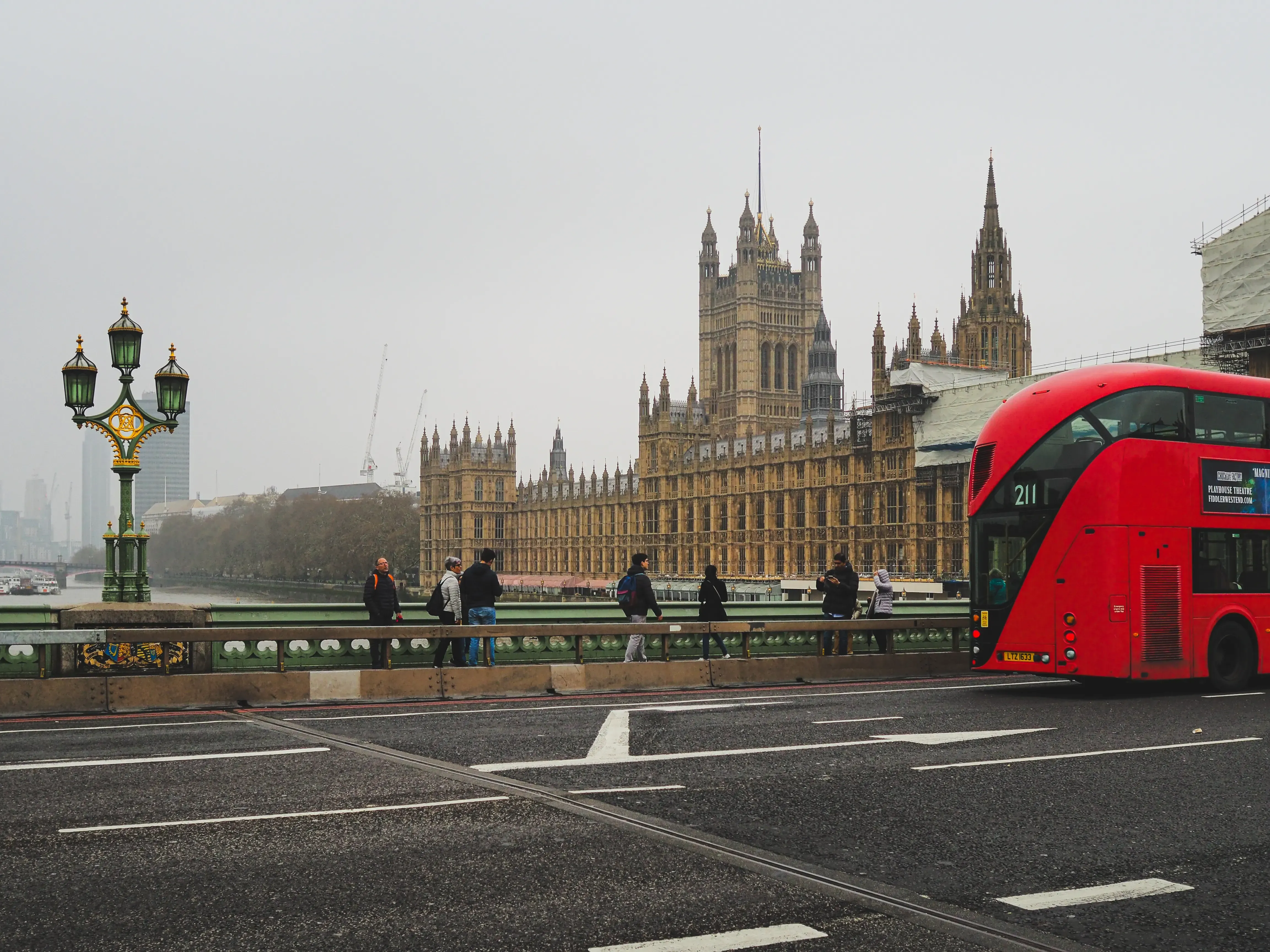 A red double-decker bus driving past the main gates of Buckingham Palace.