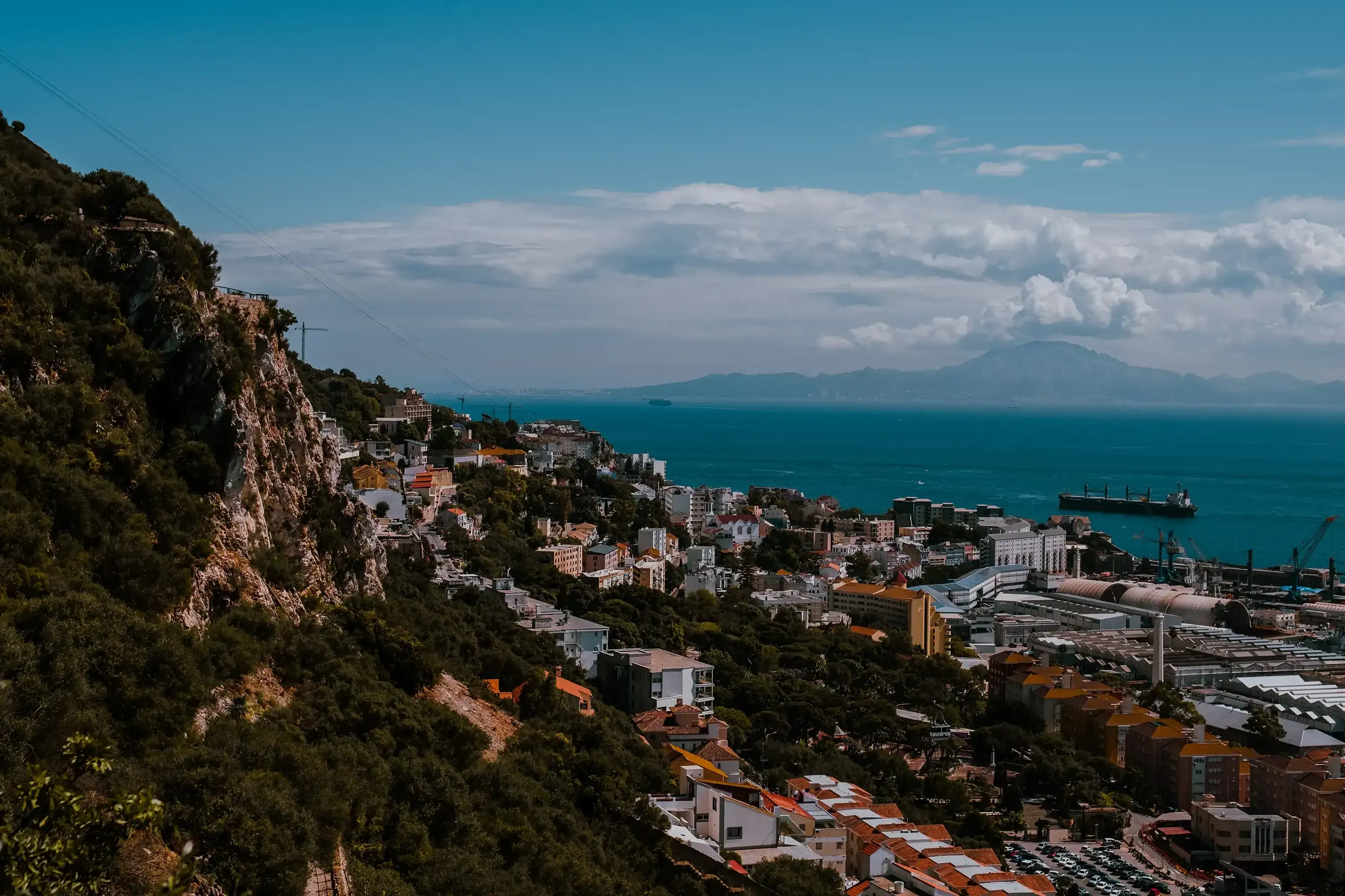 A panoramic view of the city of Gibraltar clustered at the base of the Rock, with the vast expanse of the Mediterranean Sea in the background.