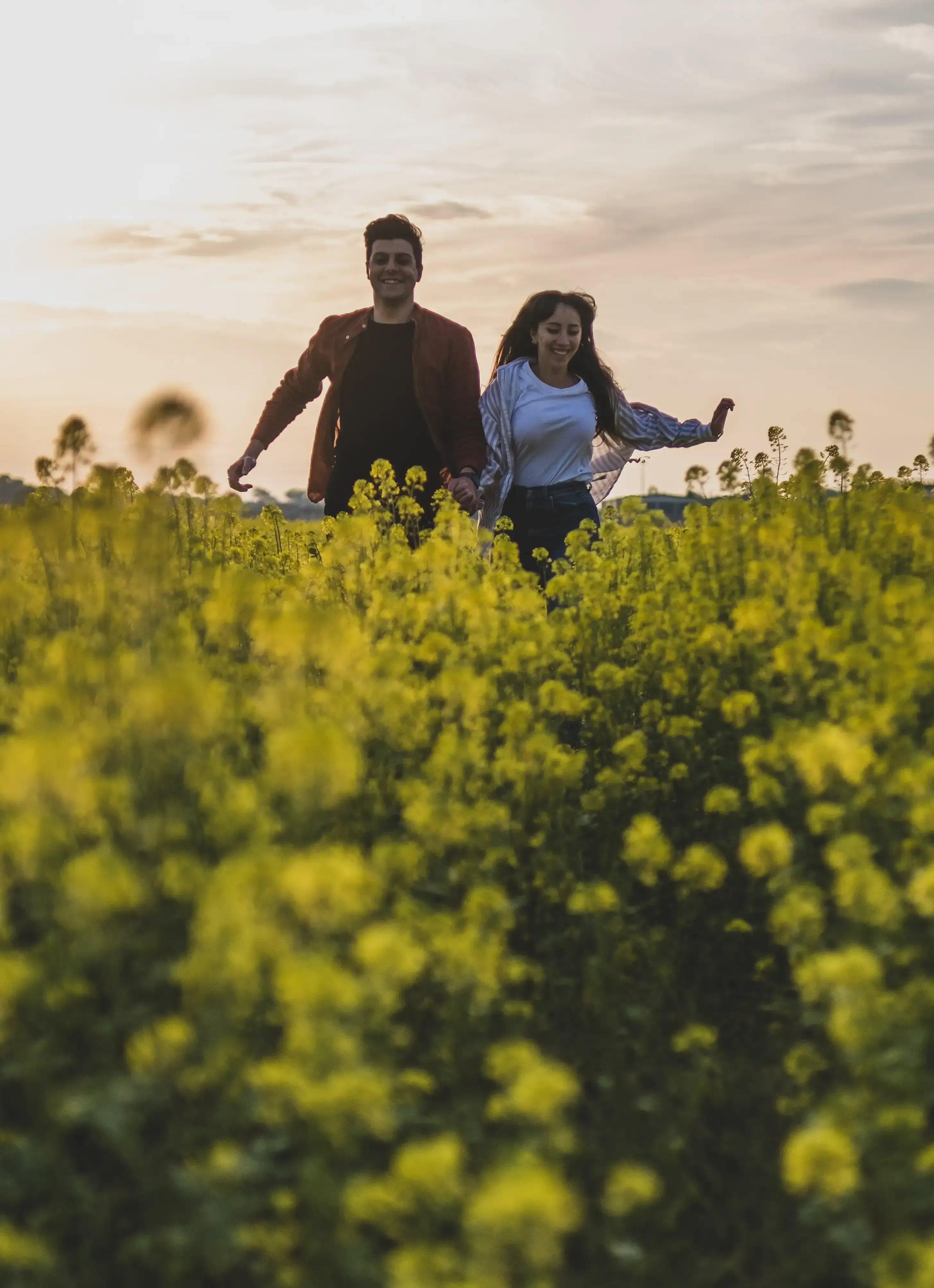 Giuseppe and Indya running together through the bright rapeseed field.