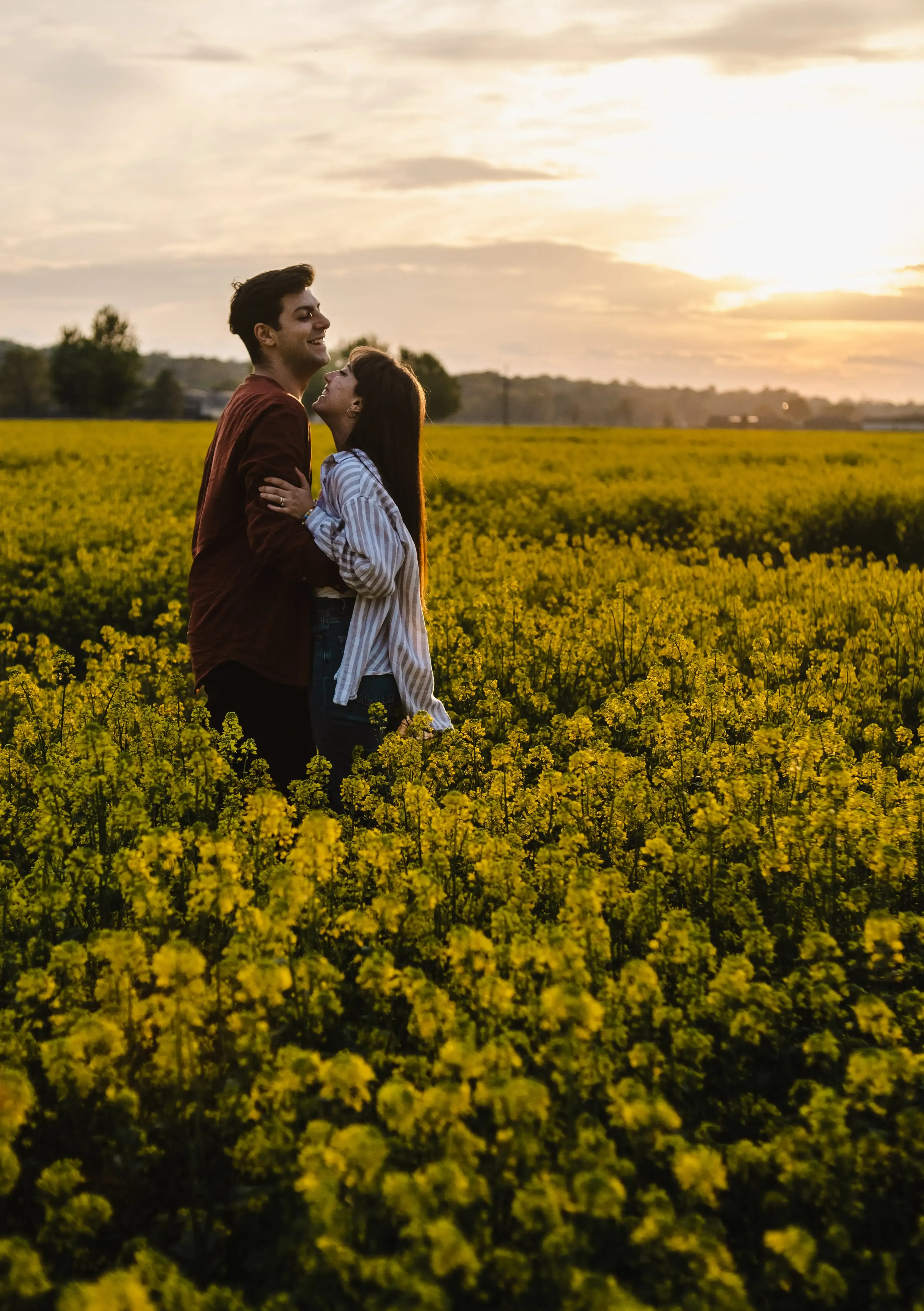 Giuseppe and Indya laughing while embracing in the yellow canola field.