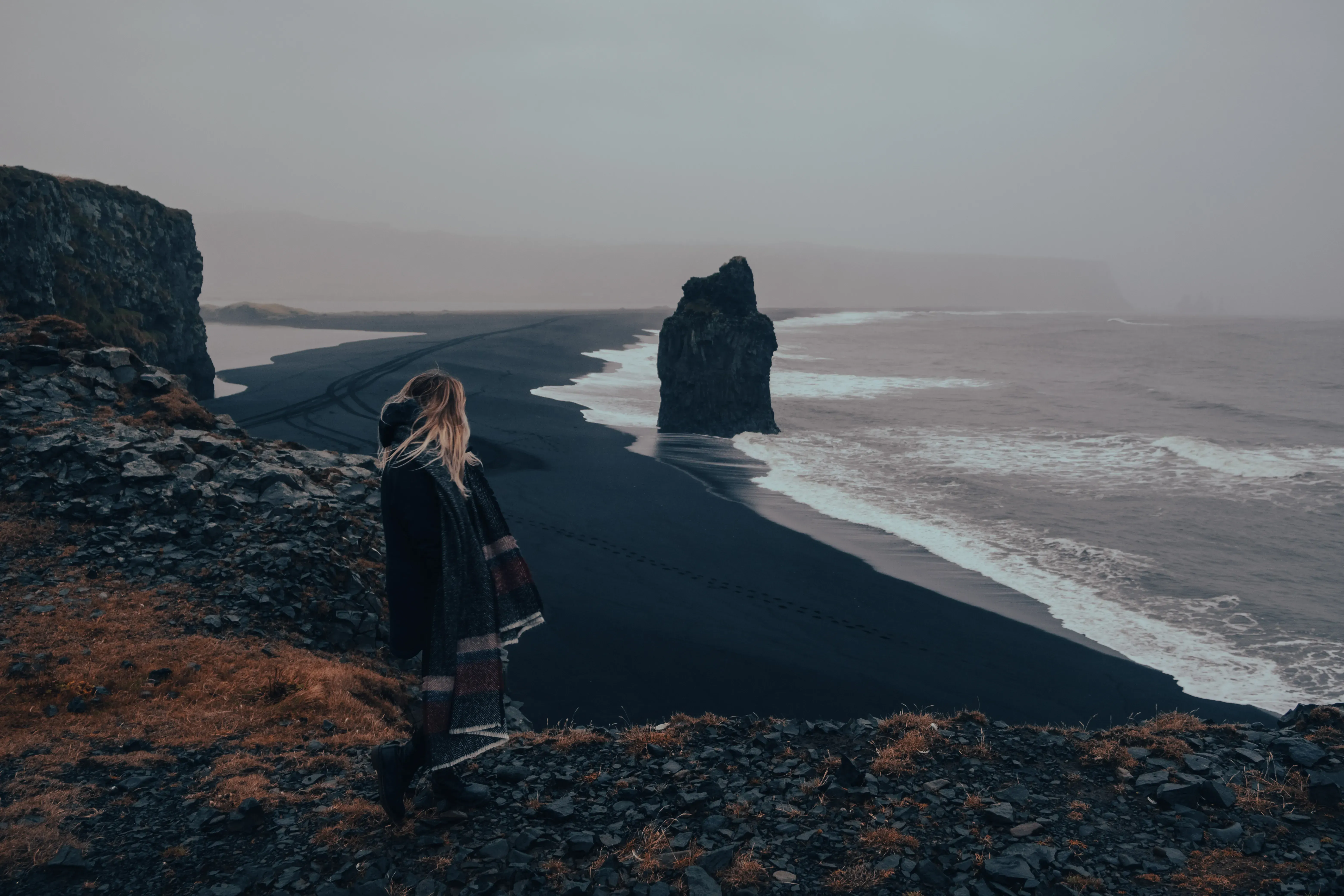 Letizia looking out over a famous black sand beach (like Reynisfjara or Diamond Beach) in Iceland.