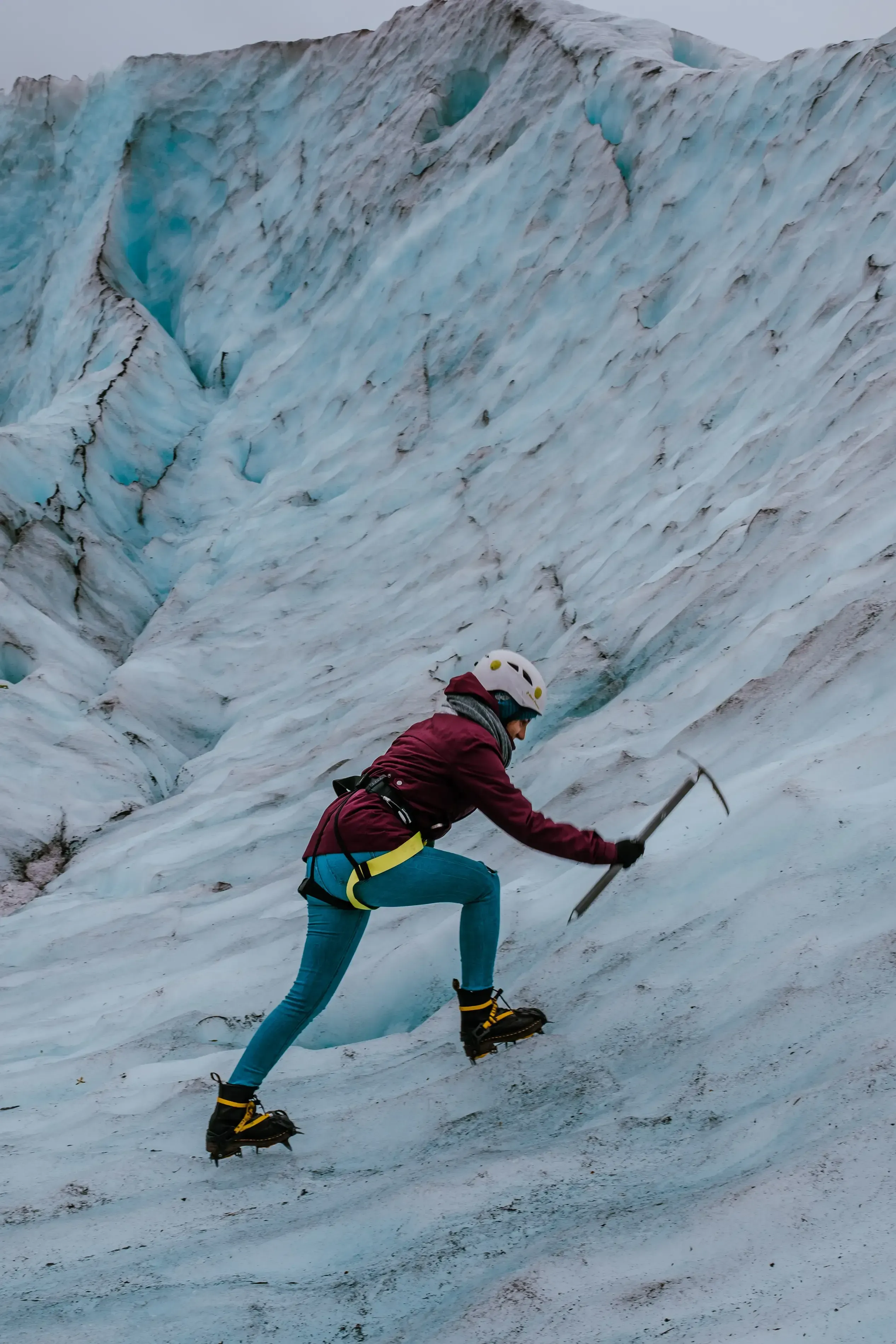 Feride climbing up a section of a glacier, equipped with ice-climbing gear.