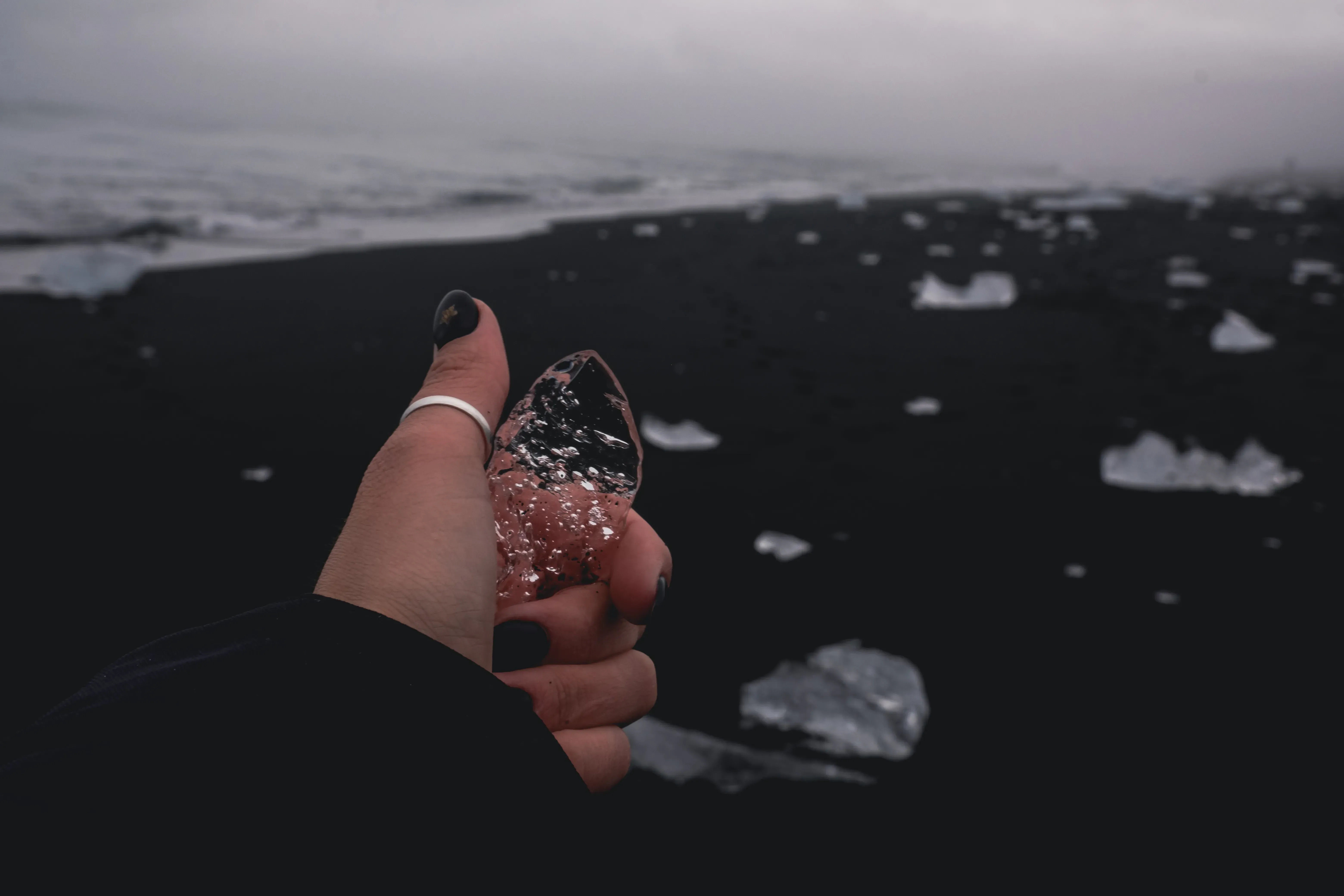 Letizia holding a small, clear piece of glacial ice on the black sand of Diamond Beach.