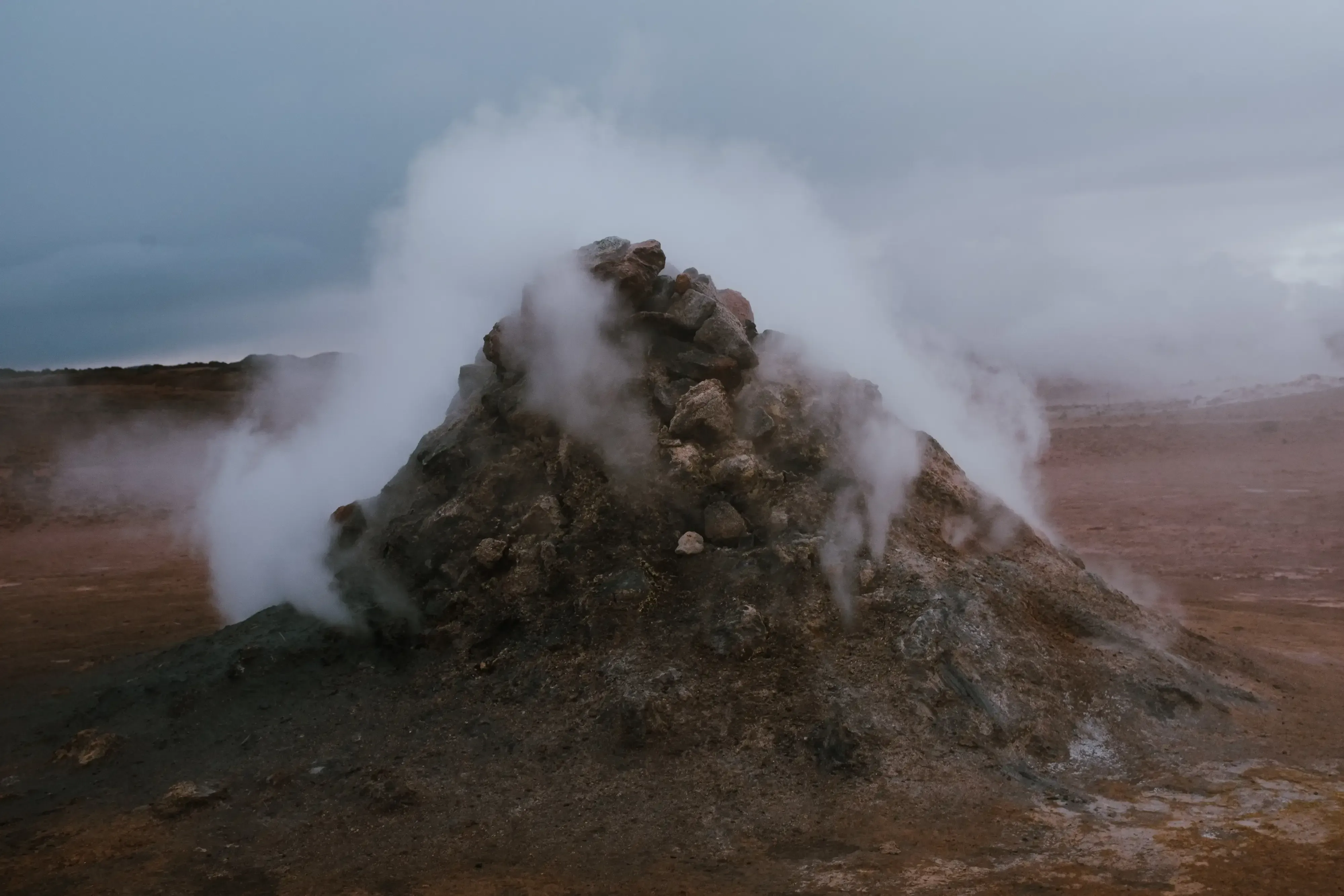 Steam and geothermal gas vents rising from the ground in a volcanic or hot spring area of Iceland.