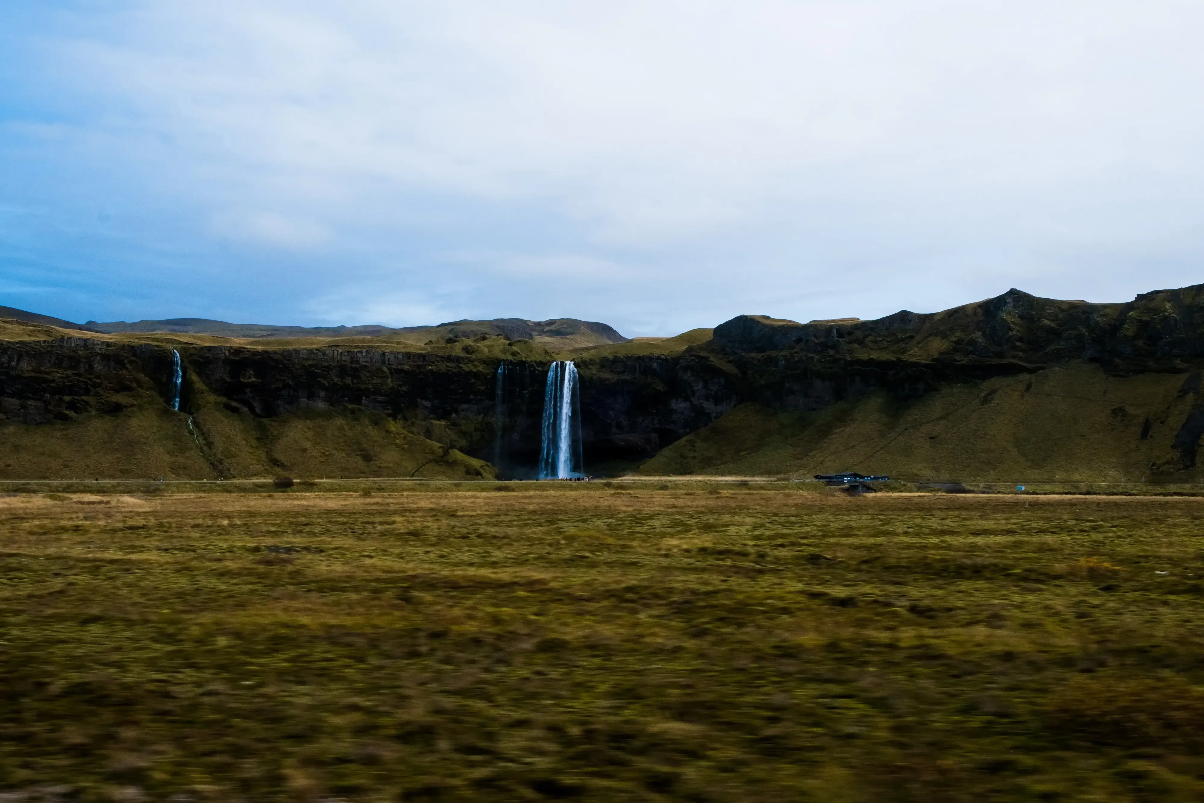 Distant view of the Seljalandsfoss waterfall, showing the full height of the water falling over the cliff edge.