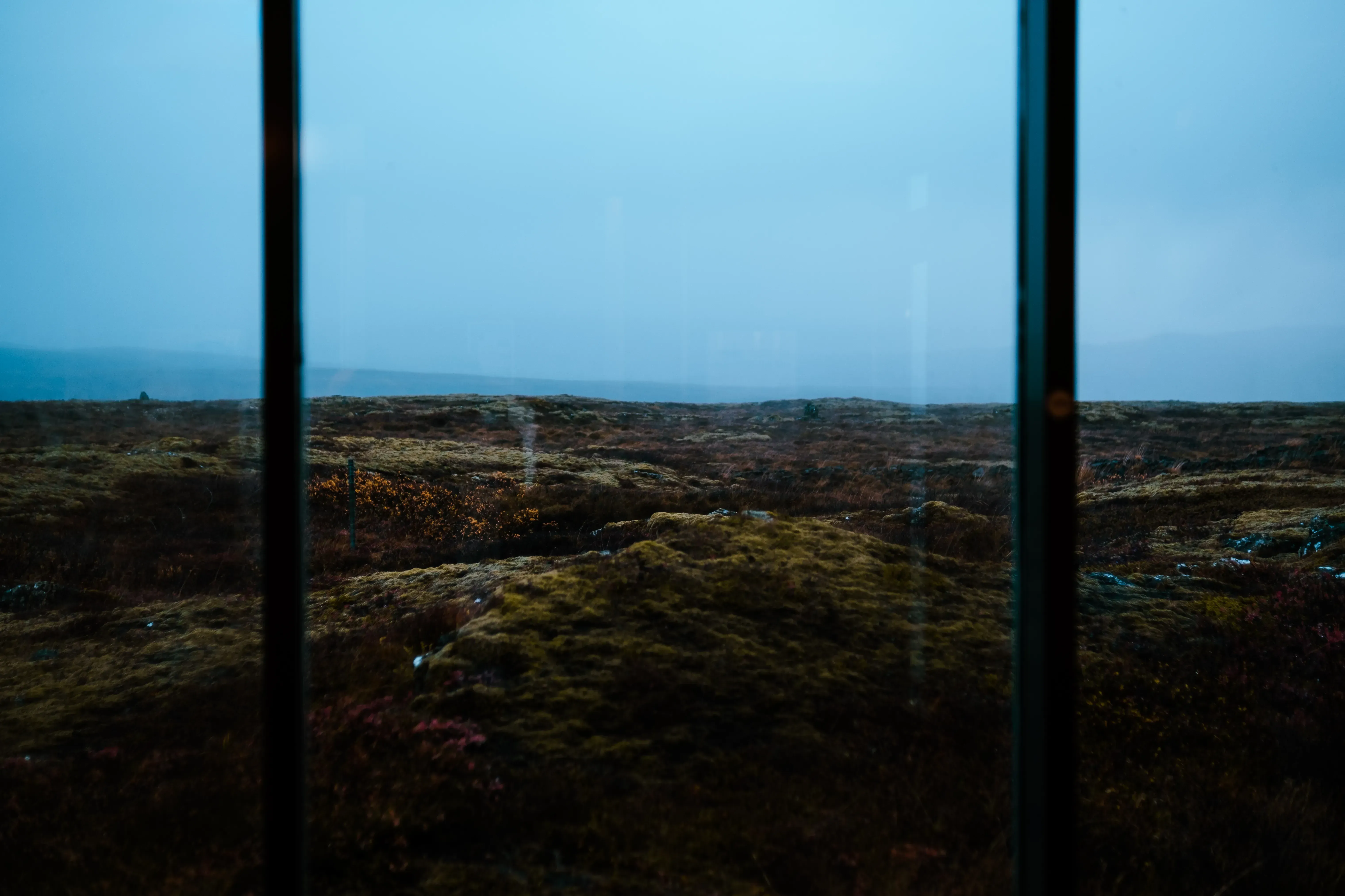 The scenic Icelandic landscape (mountains, moss, or lava fields) framed by a window.