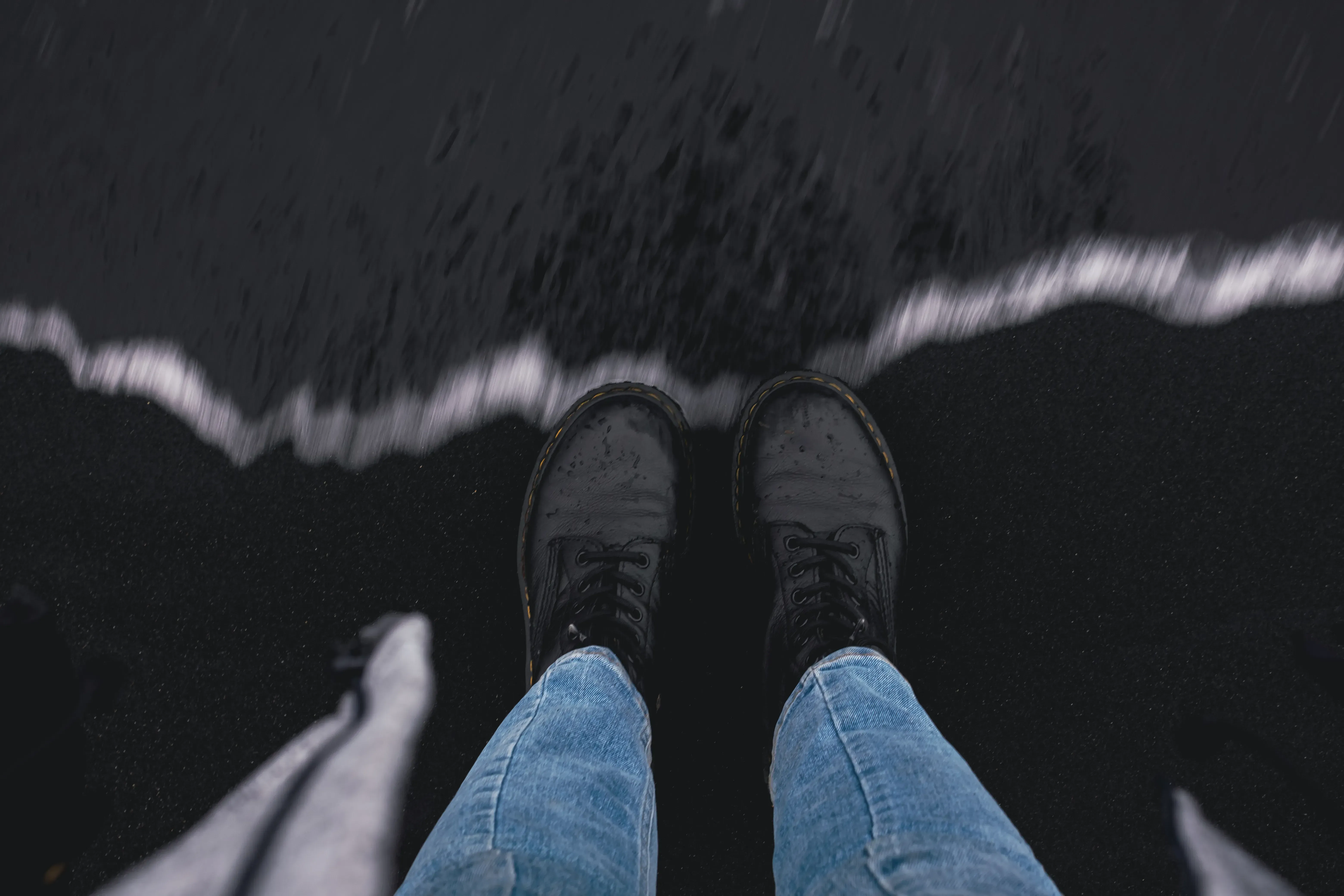 Close-up of Letizia's shoes or feet on the black sand beach (Reynisfjara) as an ocean wave approaches.