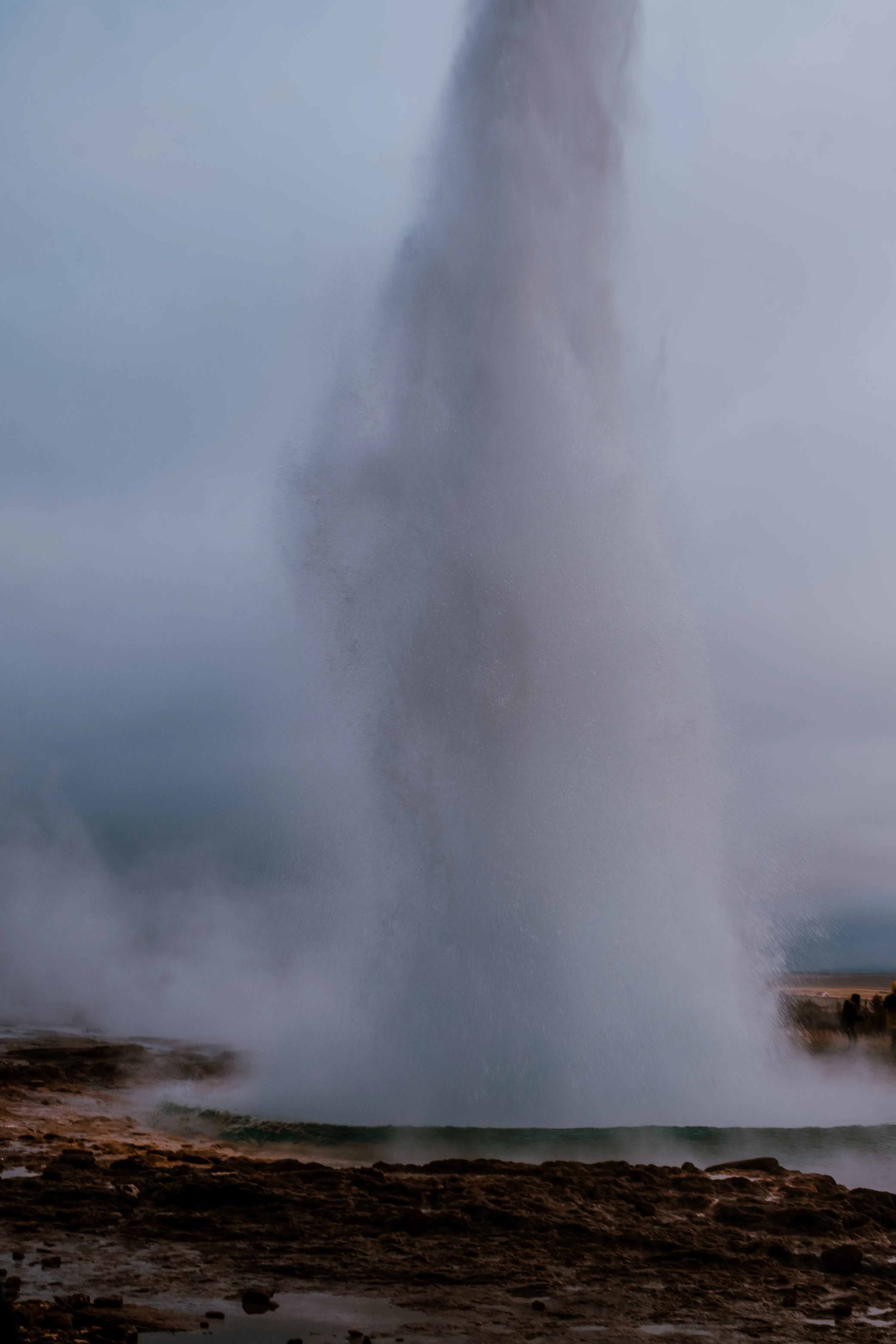 The Strokkur geyser actively erupting, shooting a high jet of steaming hot water into the air.