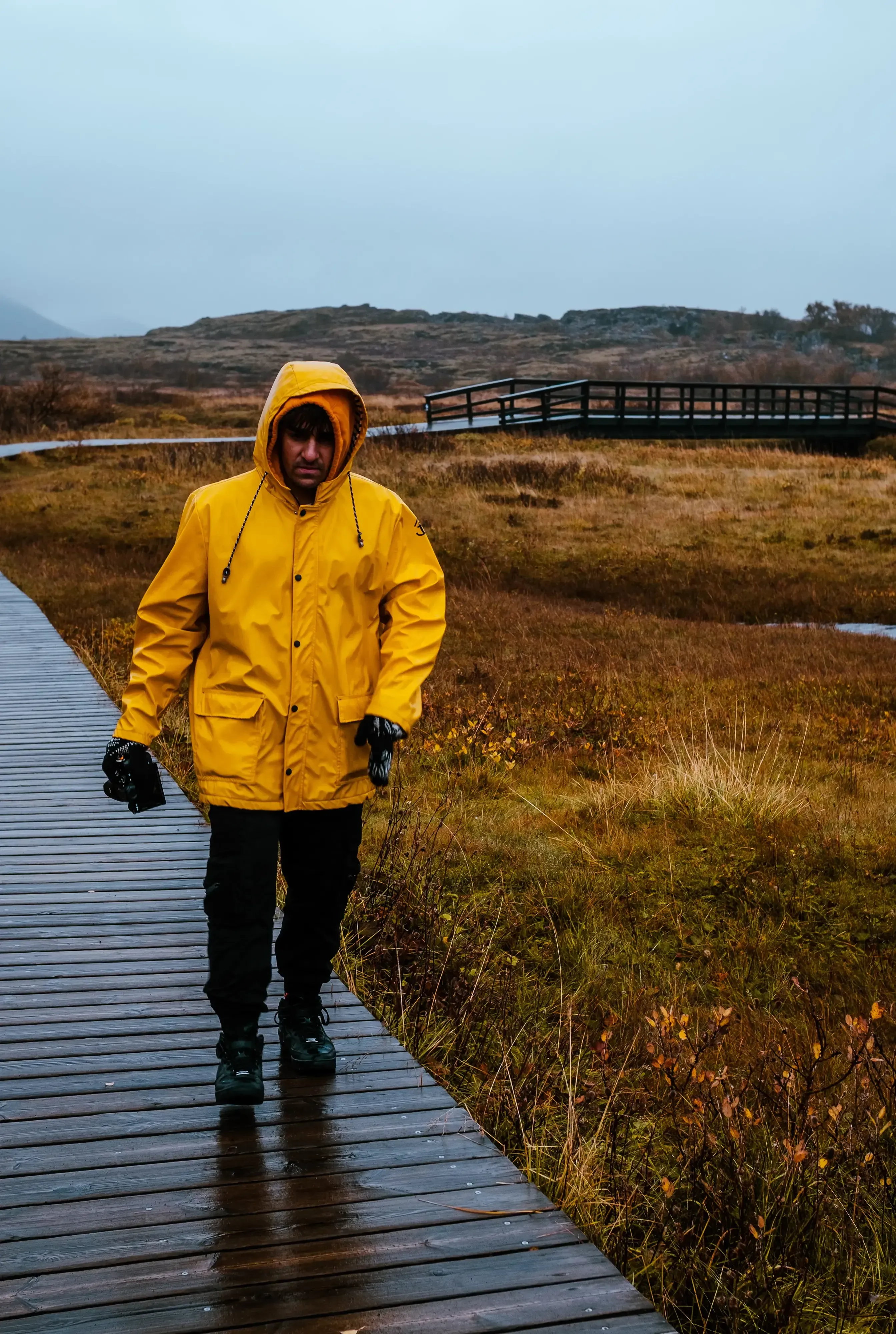 Ieser wearing a bright yellow waterproof coat, walking along a raised wooden boardwalk or pathway.