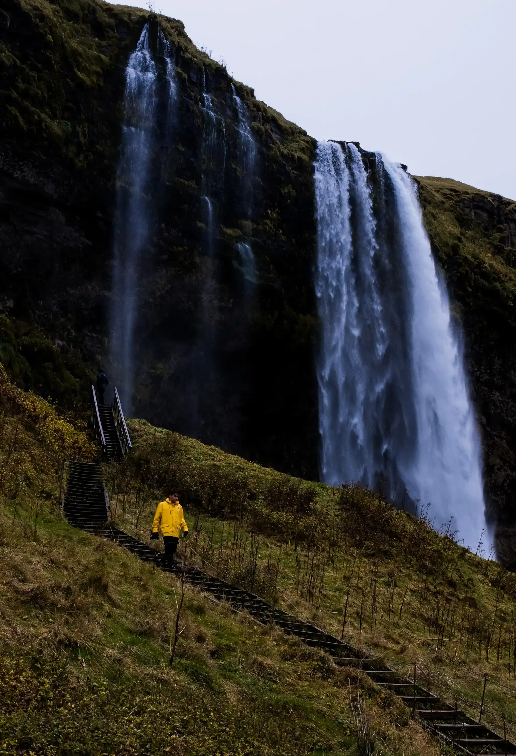Ieser walking along the path or field, approaching the base of the Seljalandsfoss waterfall.
