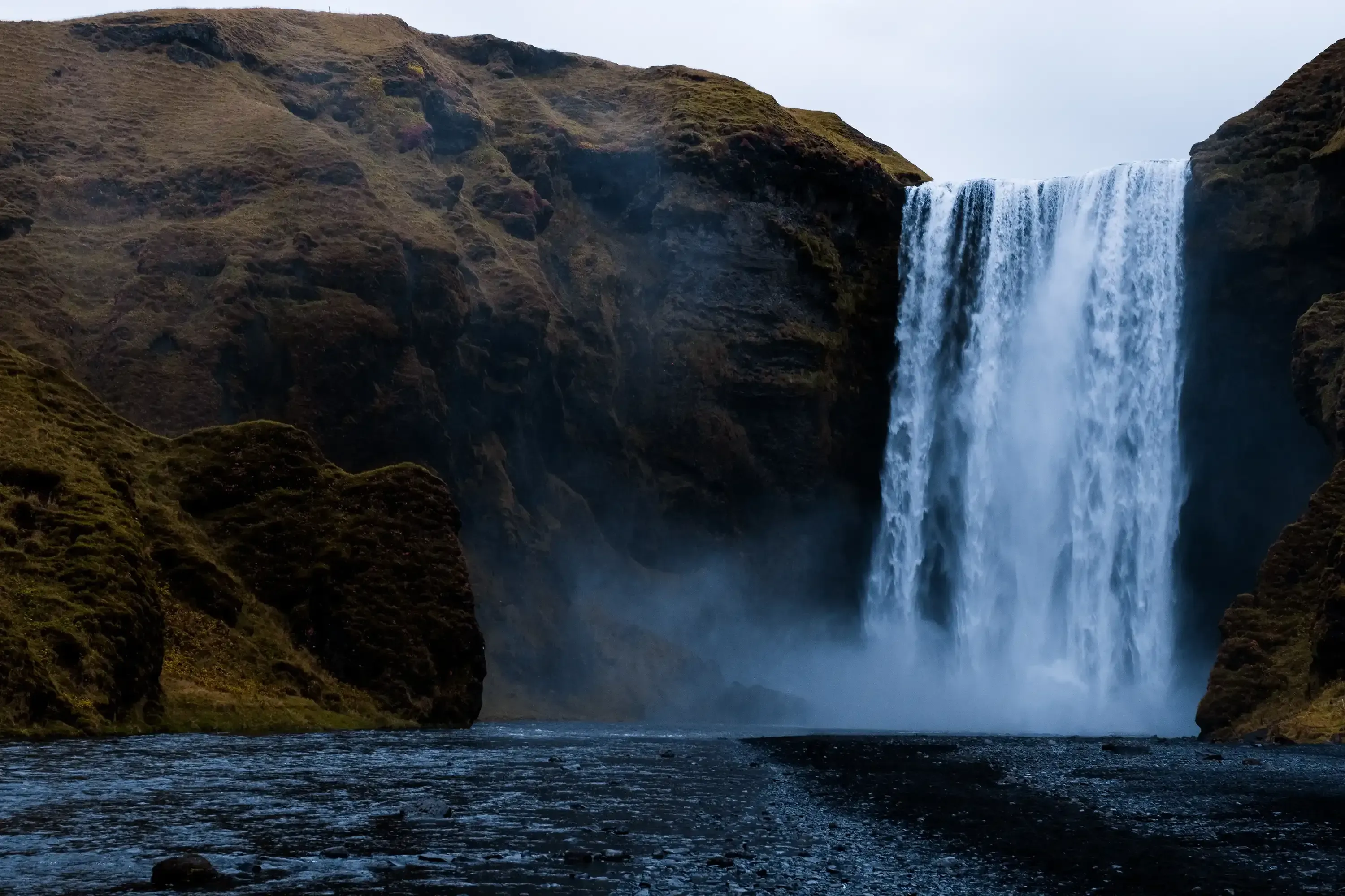 The massive Skógafoss waterfall viewed from the base, emphasizing its height and the pool below.