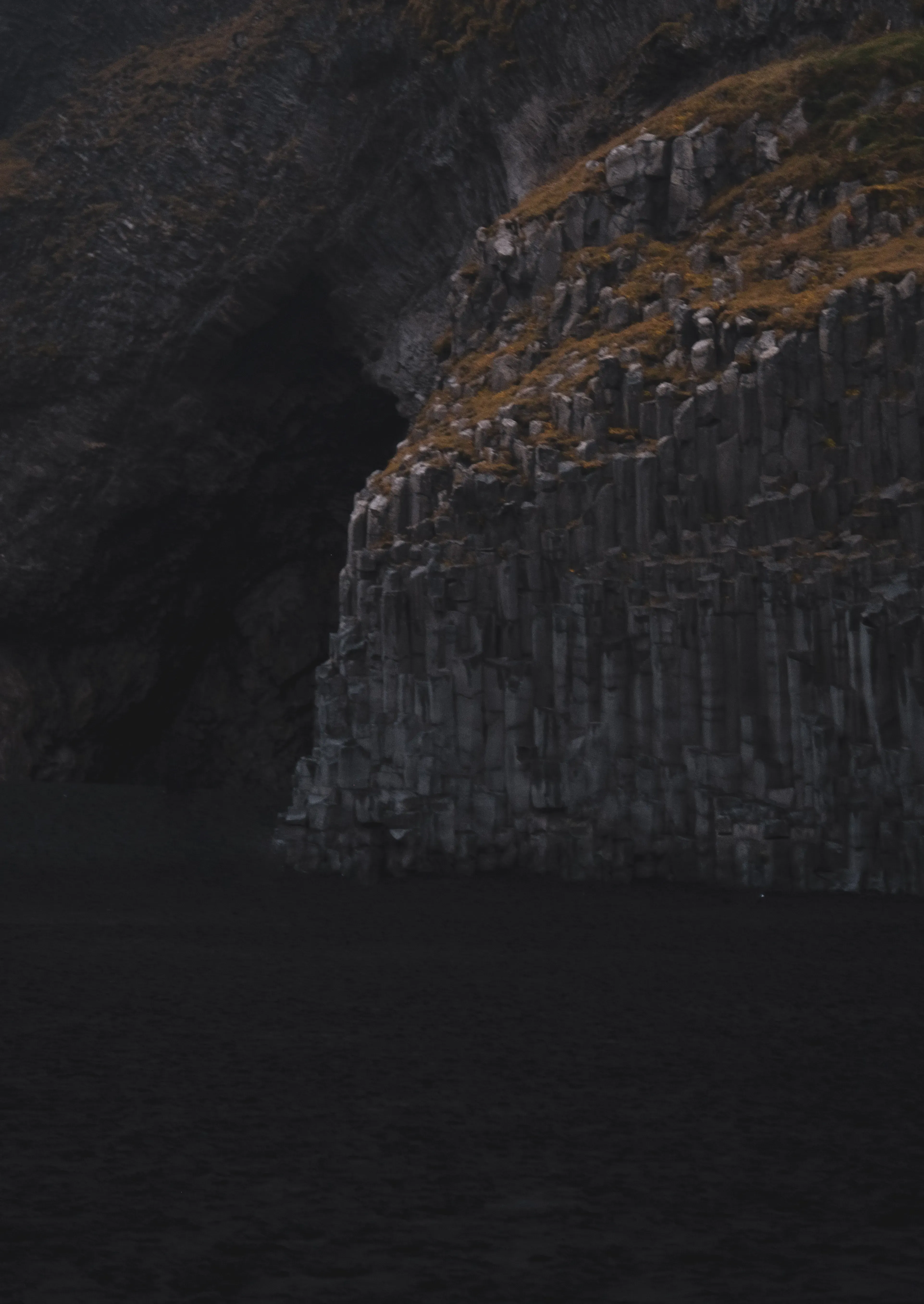 An expansive view of a volcanic black sand beach (like Reynisfjara) with dark sand and ocean waves.