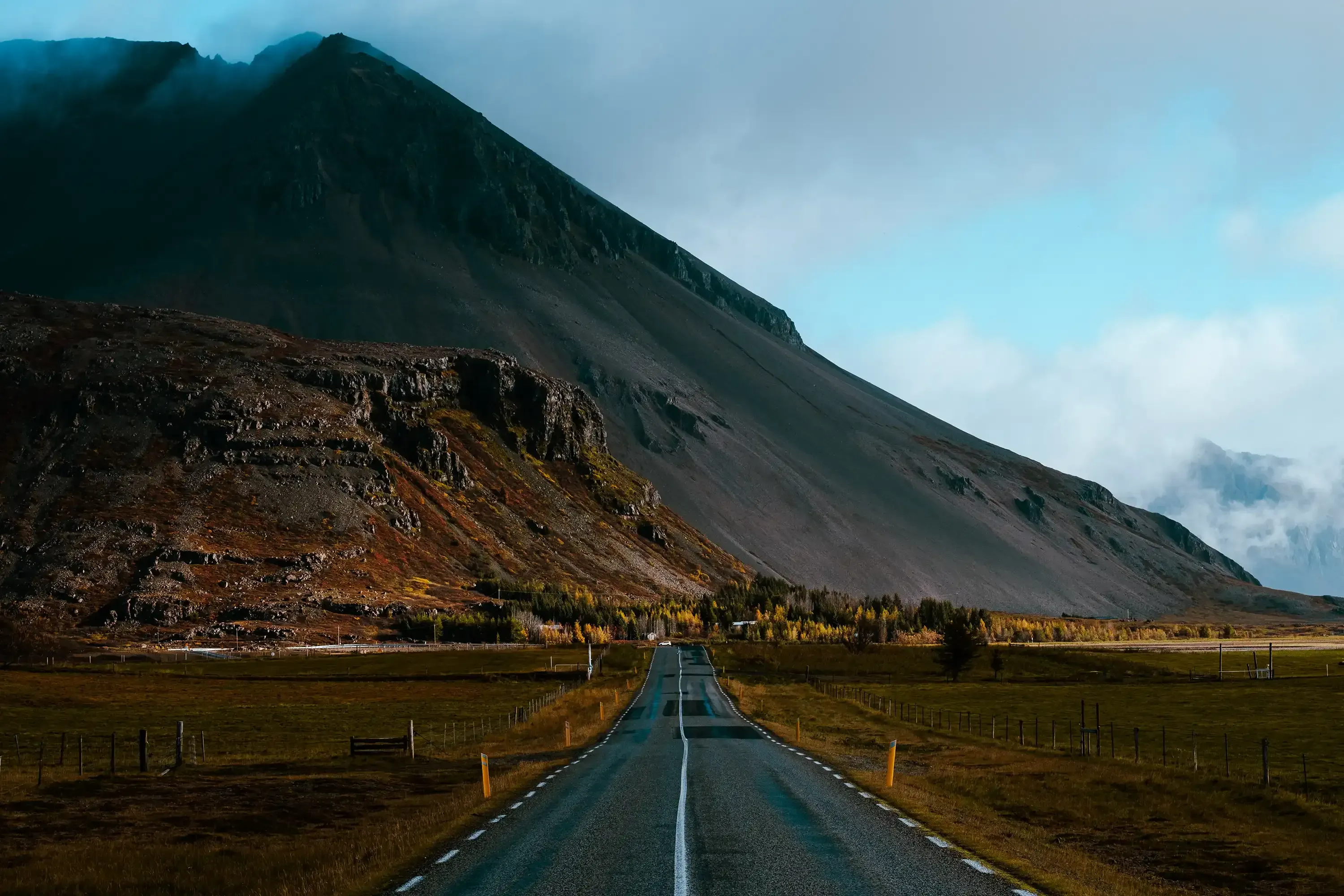 A straight road stretching across the Icelandic countryside with distant mountains in the background.ù