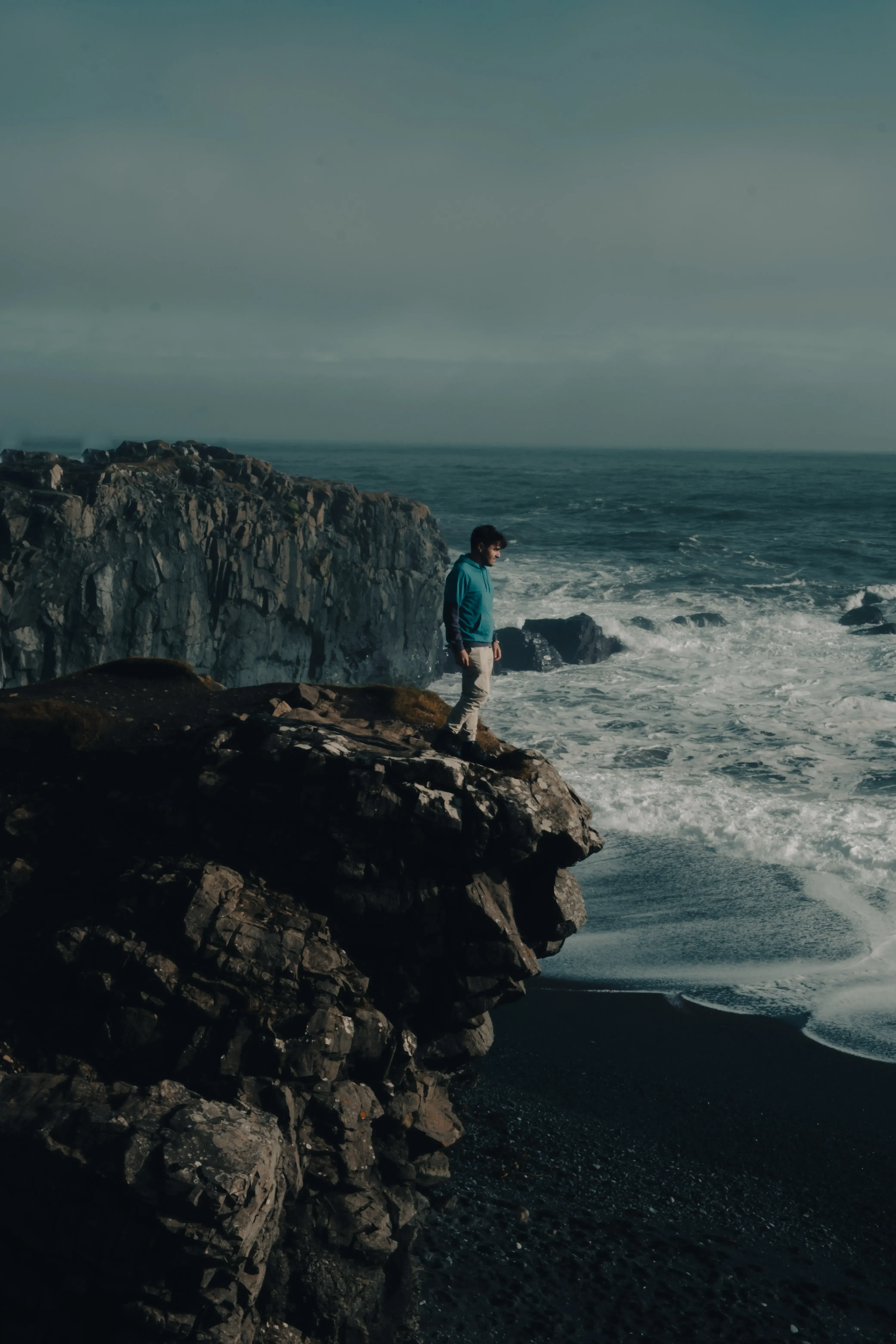 Ieser standing on a dramatic, coastal cliff edge overlooking the ocean in Iceland.