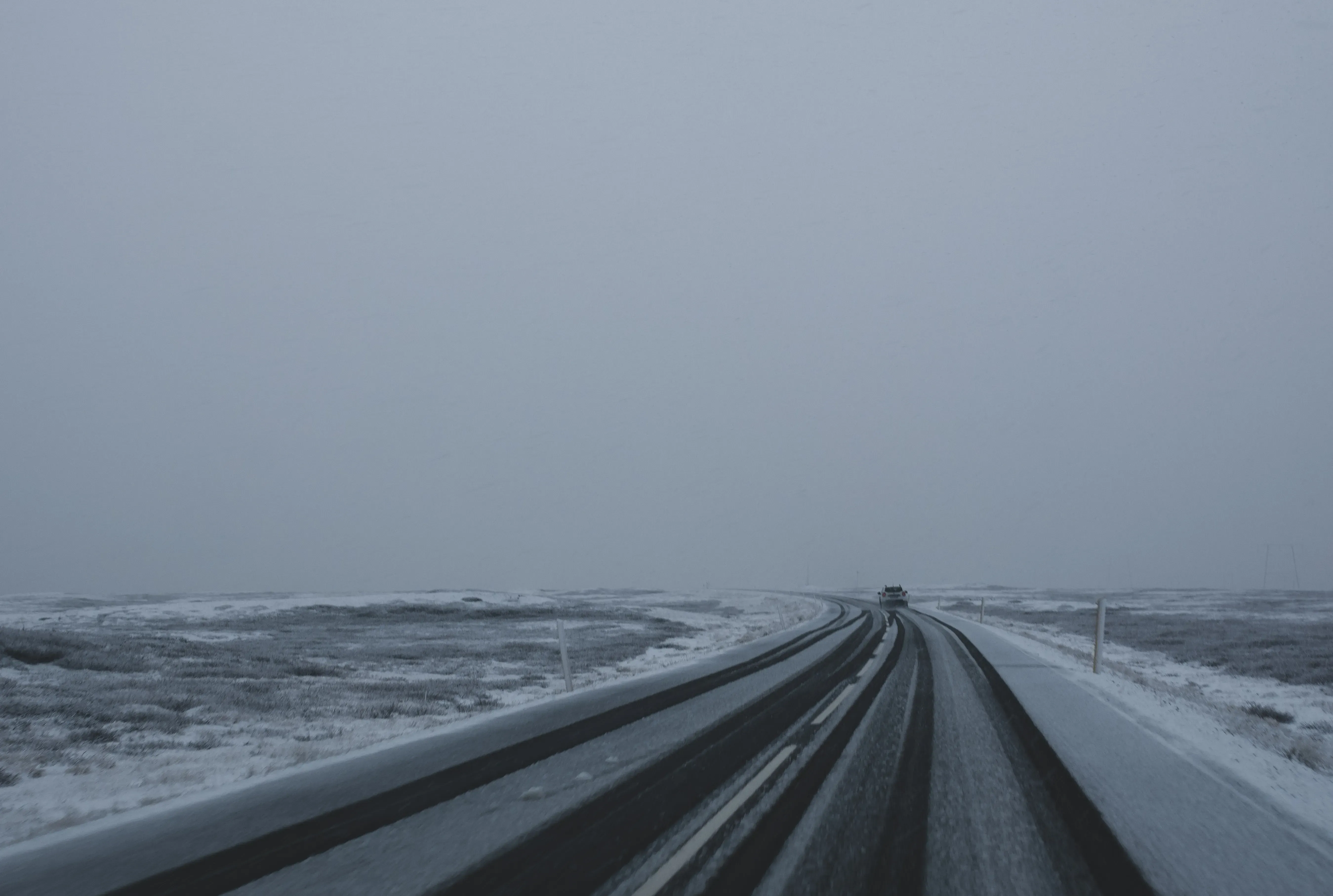 A road partially covered with snow, surrounded by a wintery Icelandic scene.