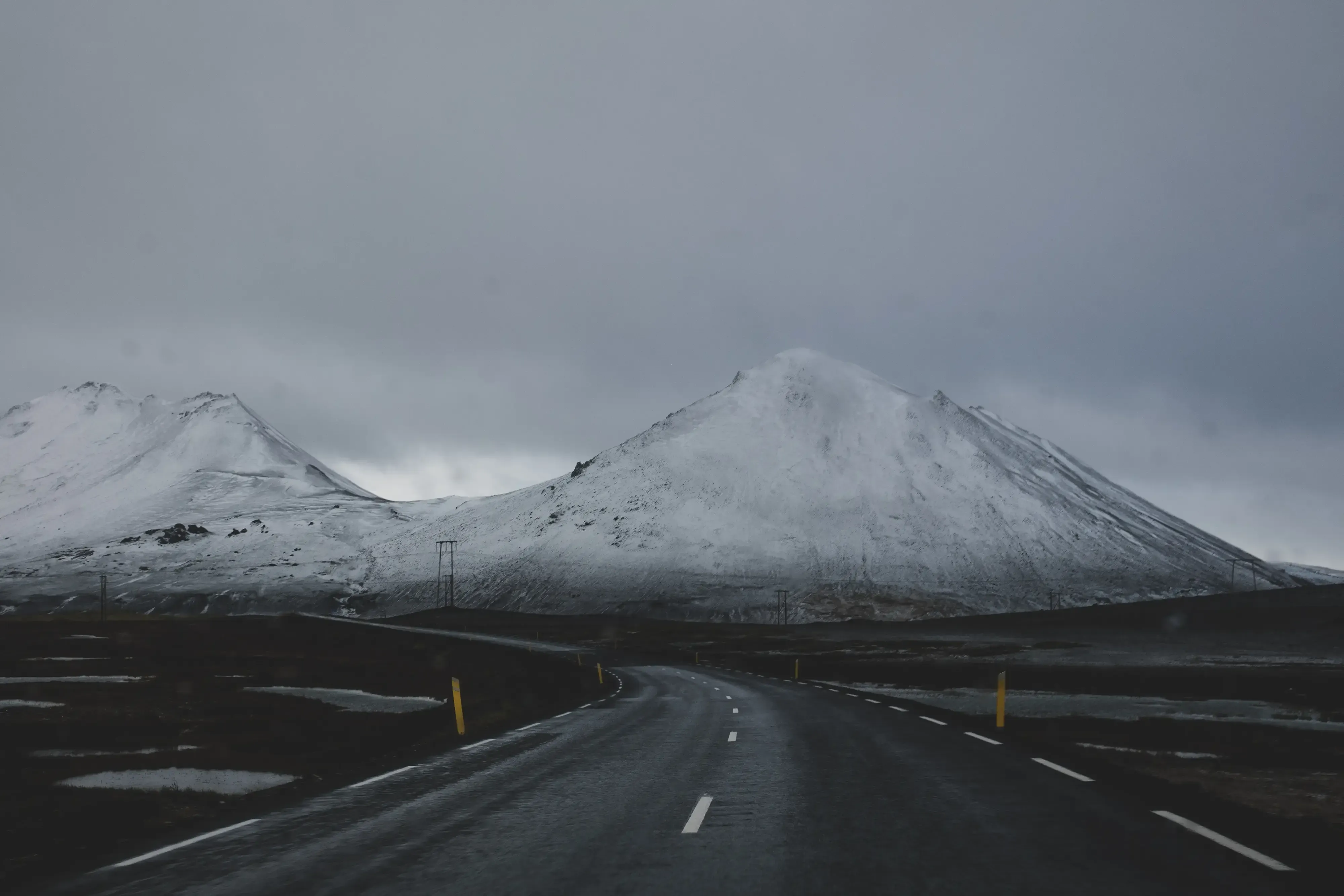 A flat road running through the Icelandic plains, with large mountains visible in the background.