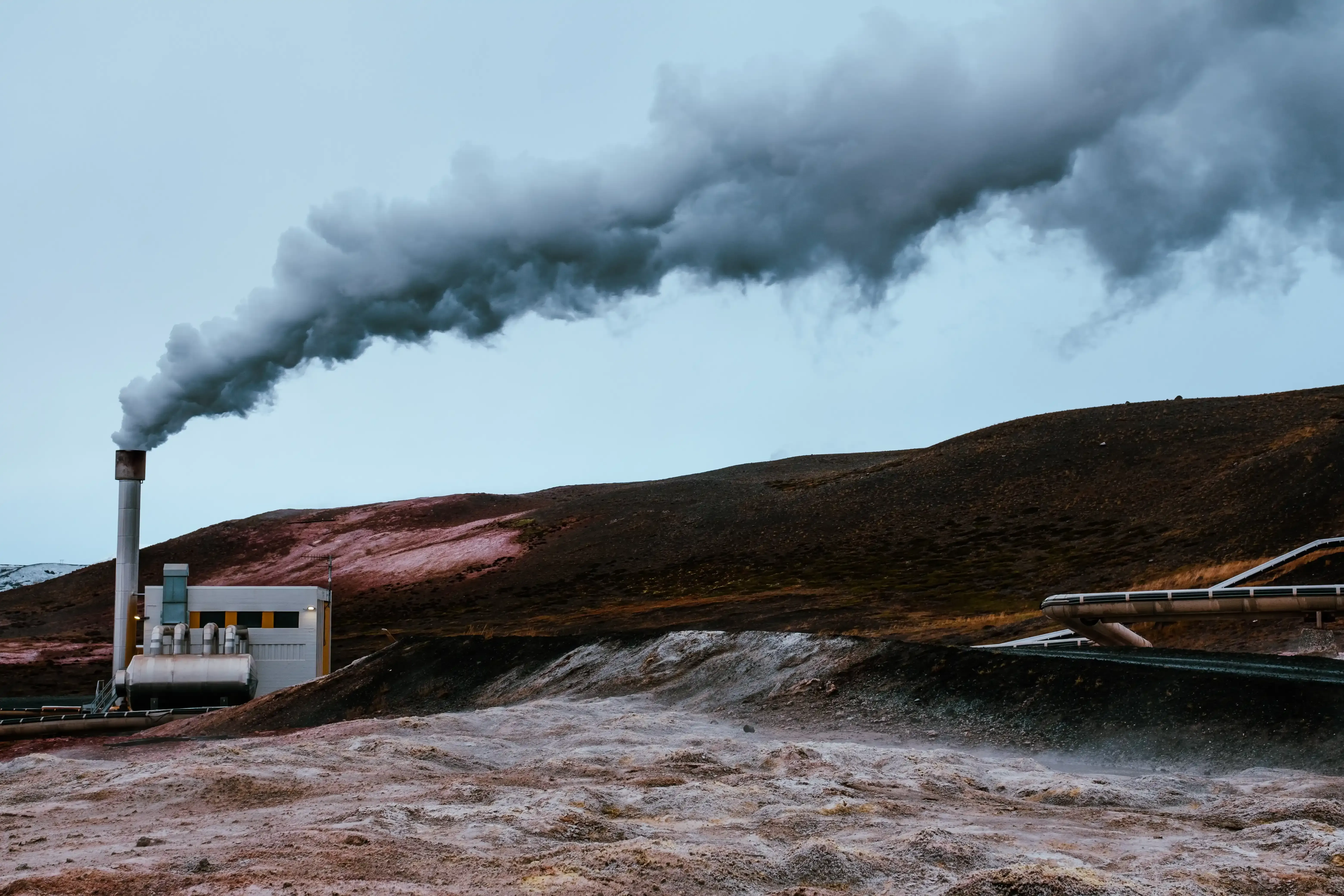 A wide view of an active geothermal power plant facility in Iceland, releasing steam.
