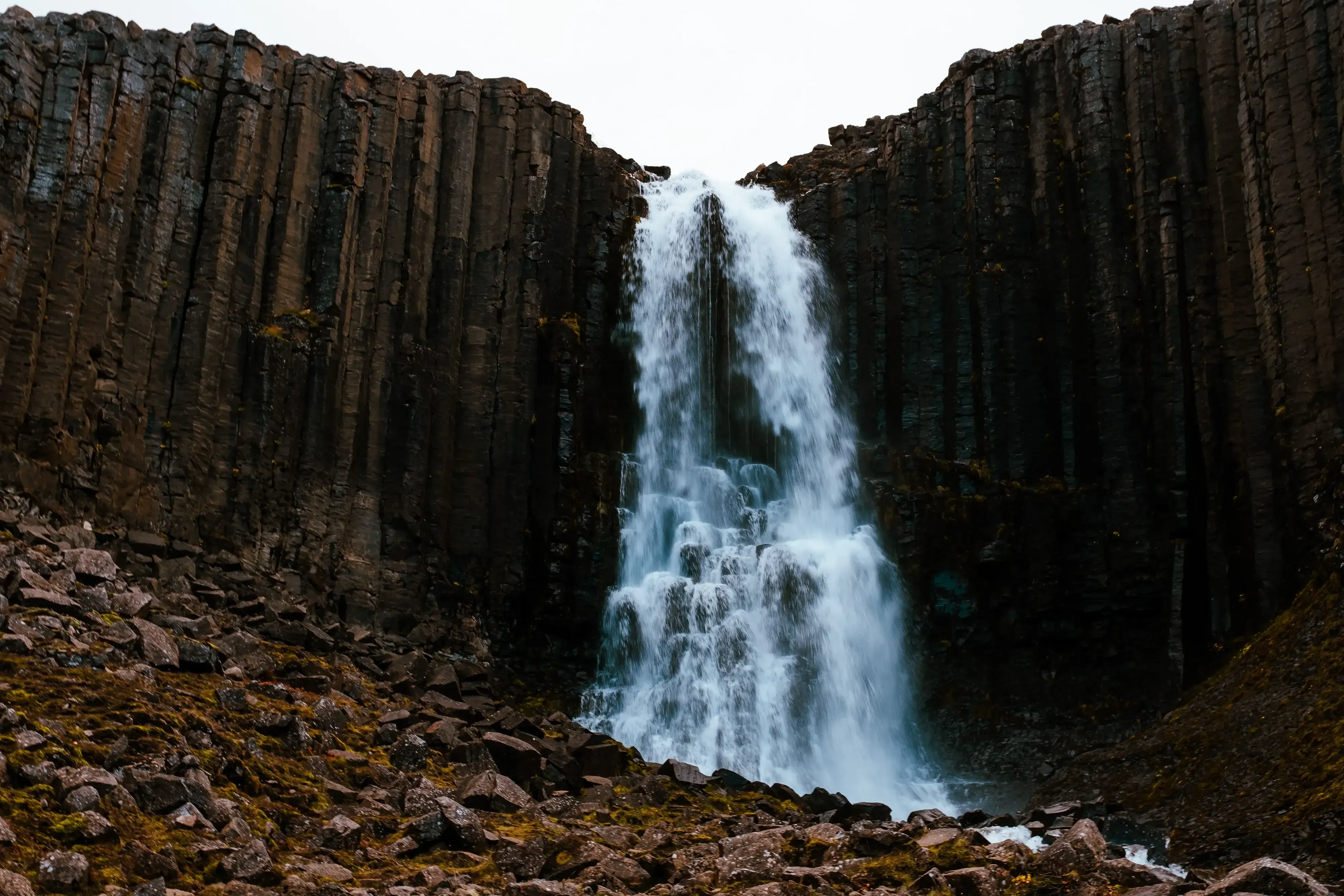 Water cascading over a cliff face composed of dark, hexagonal basalt columns.