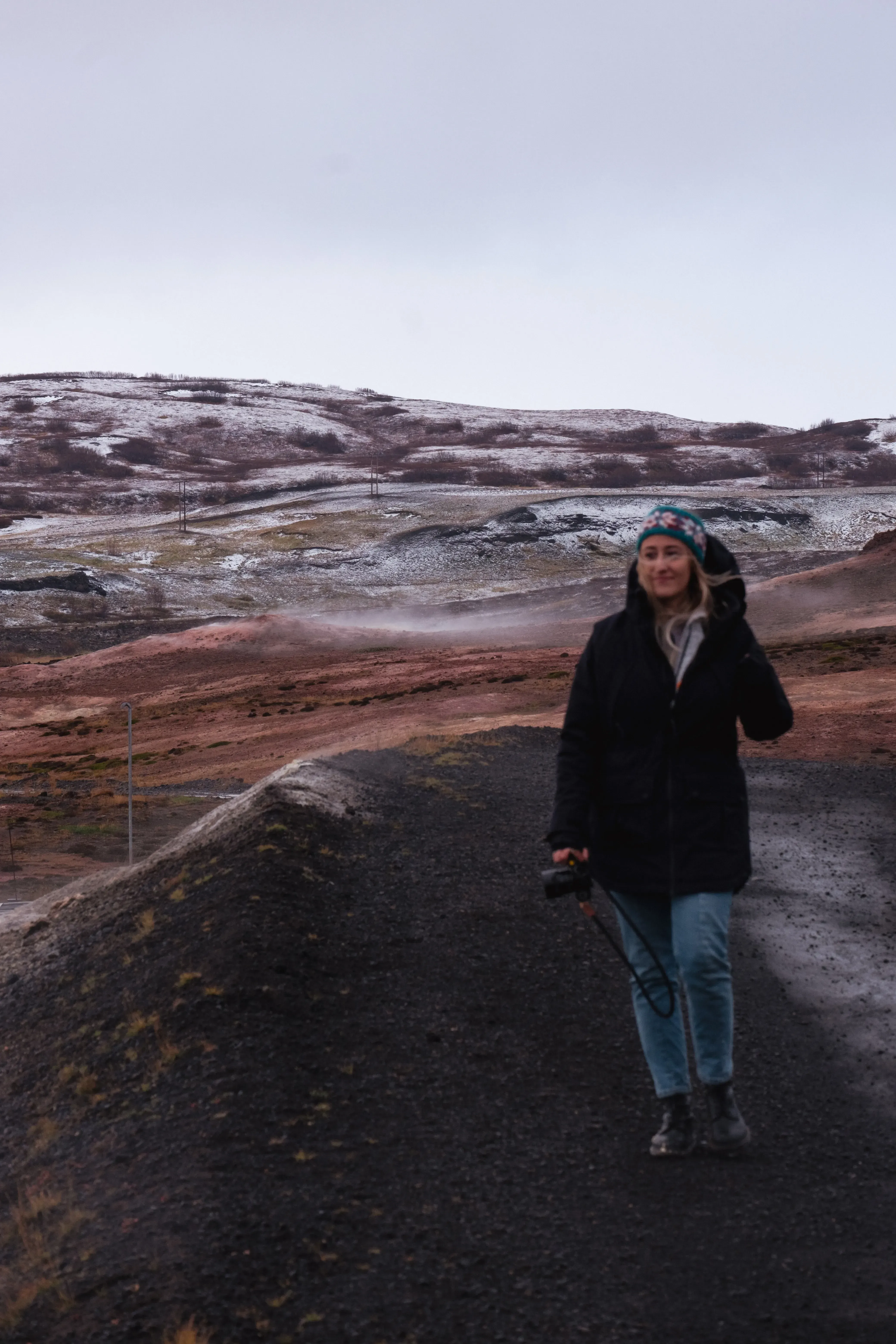 Letizia walking through a geothermal area where steam and vapor are visibly rising from the ground.
