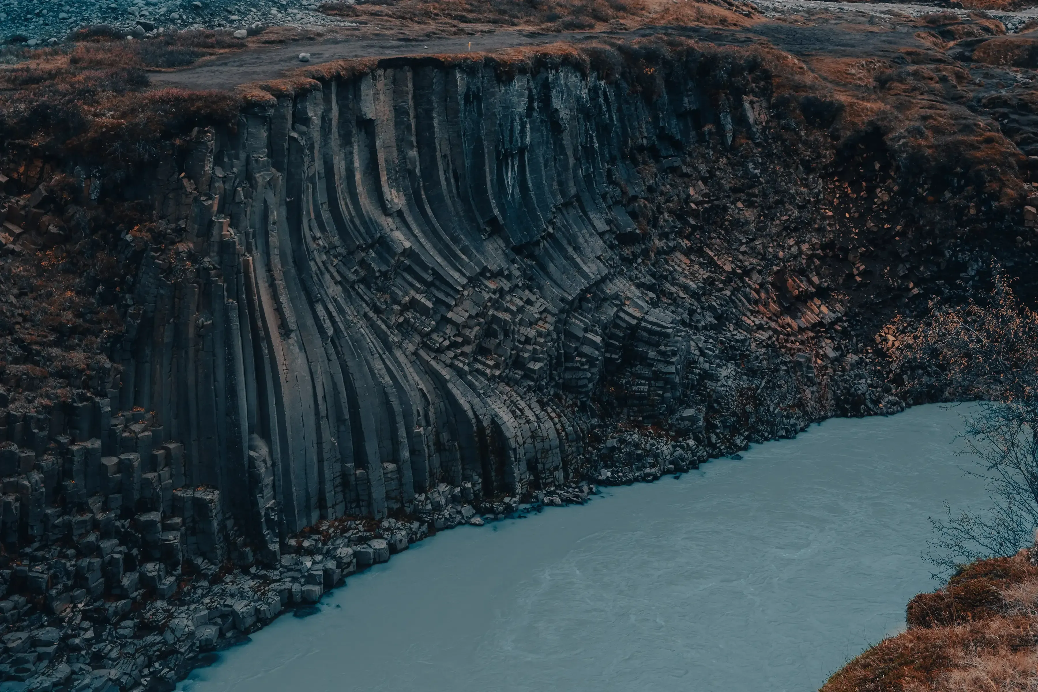 The river flowing alongside the towering basalt rock formations within Stuðlagil Canyon.