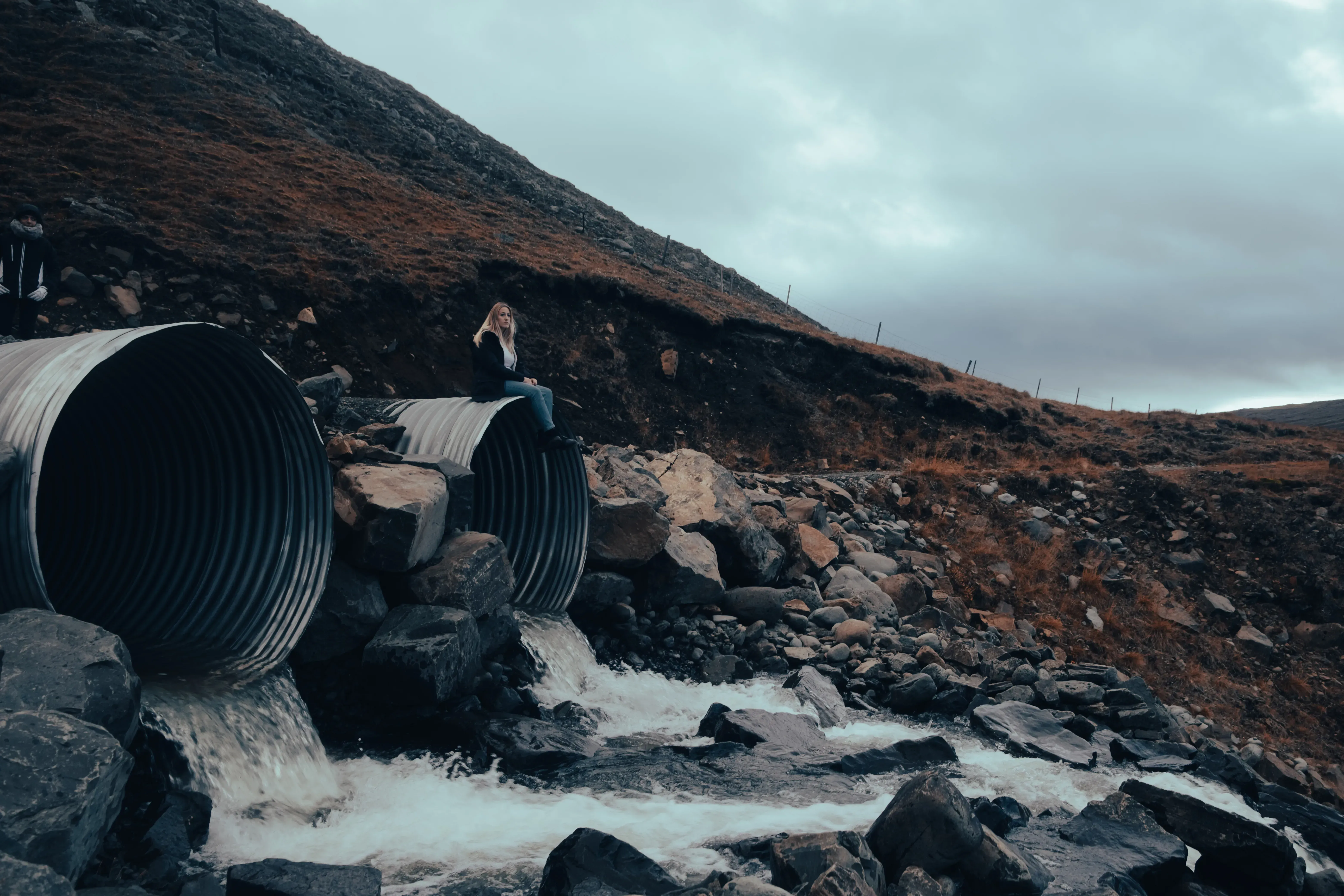 Letizia sitting on a large pipe or culvert crossing over or under a river in the landscape.