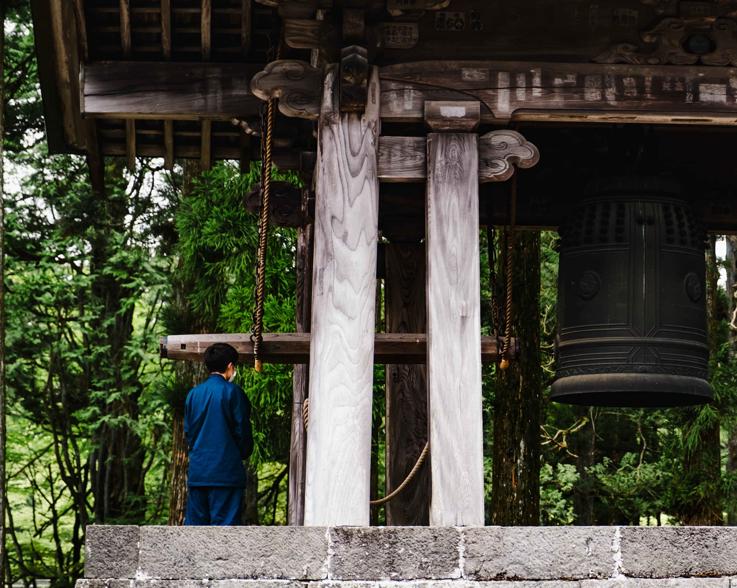 A boy preparing to strike a large temple bell with a wooden beam in Nikko