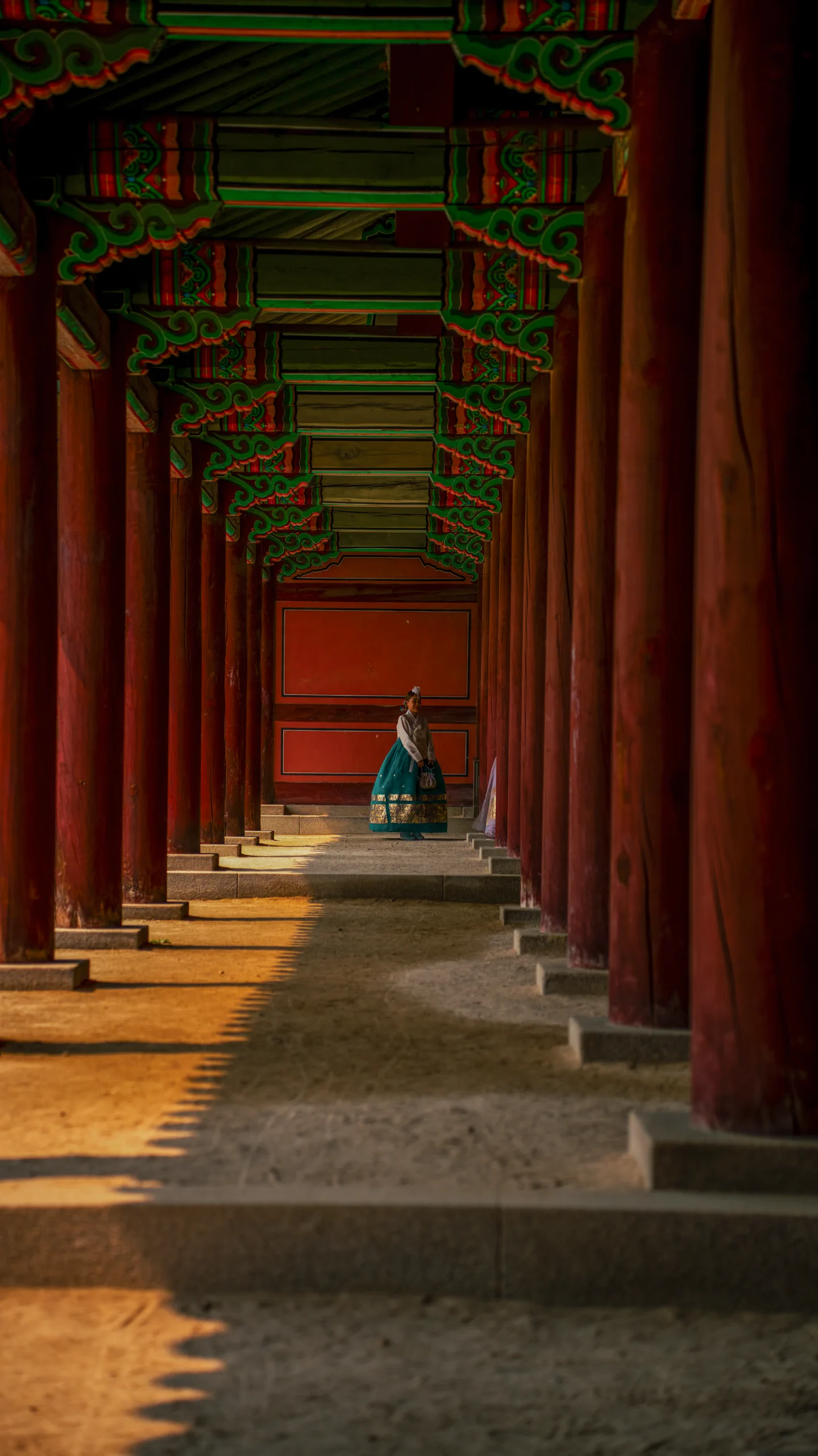 Woman in a traditional Hanbok dress standing at the end of a columned hall in the Gyeongbokgung Palace