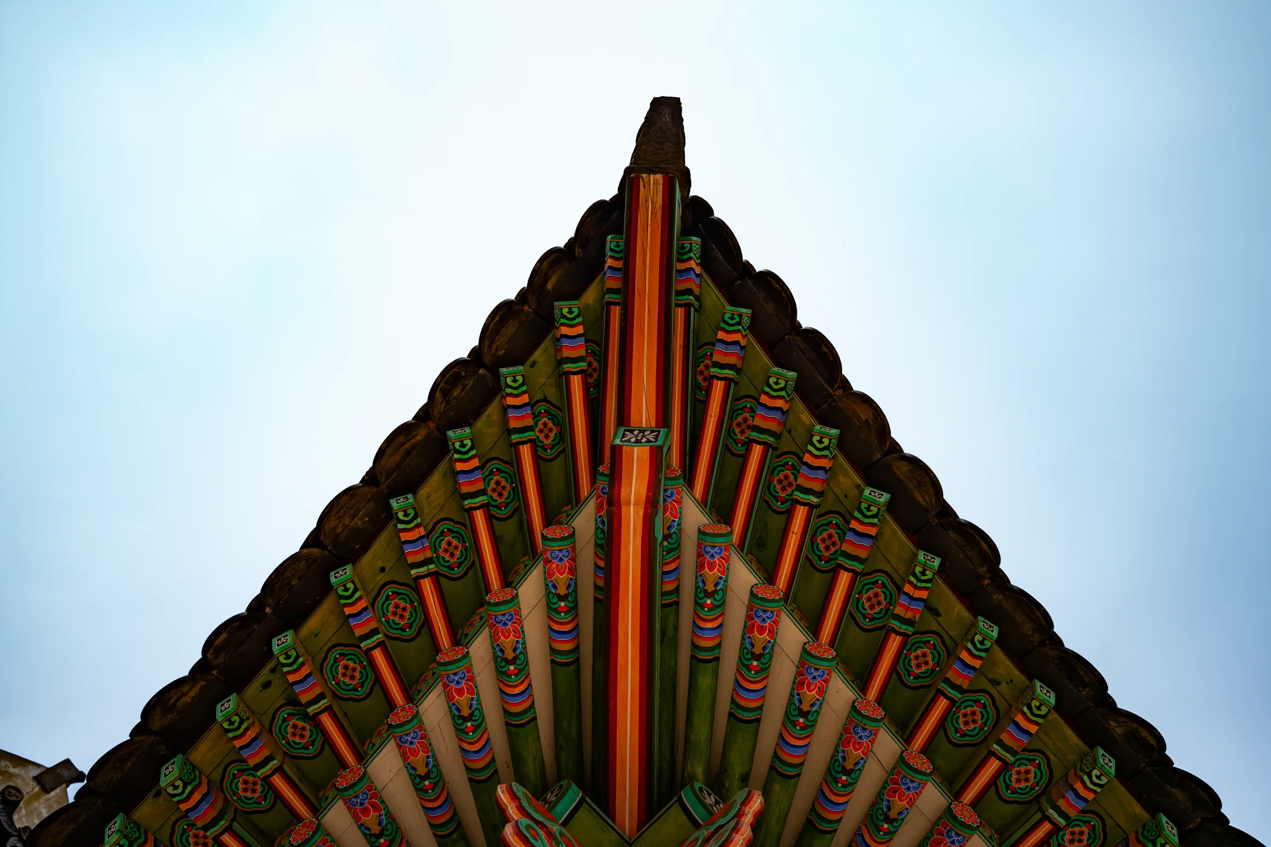 Detail of a curved, traditional Korean roof corner (dancheong) against the sky.
