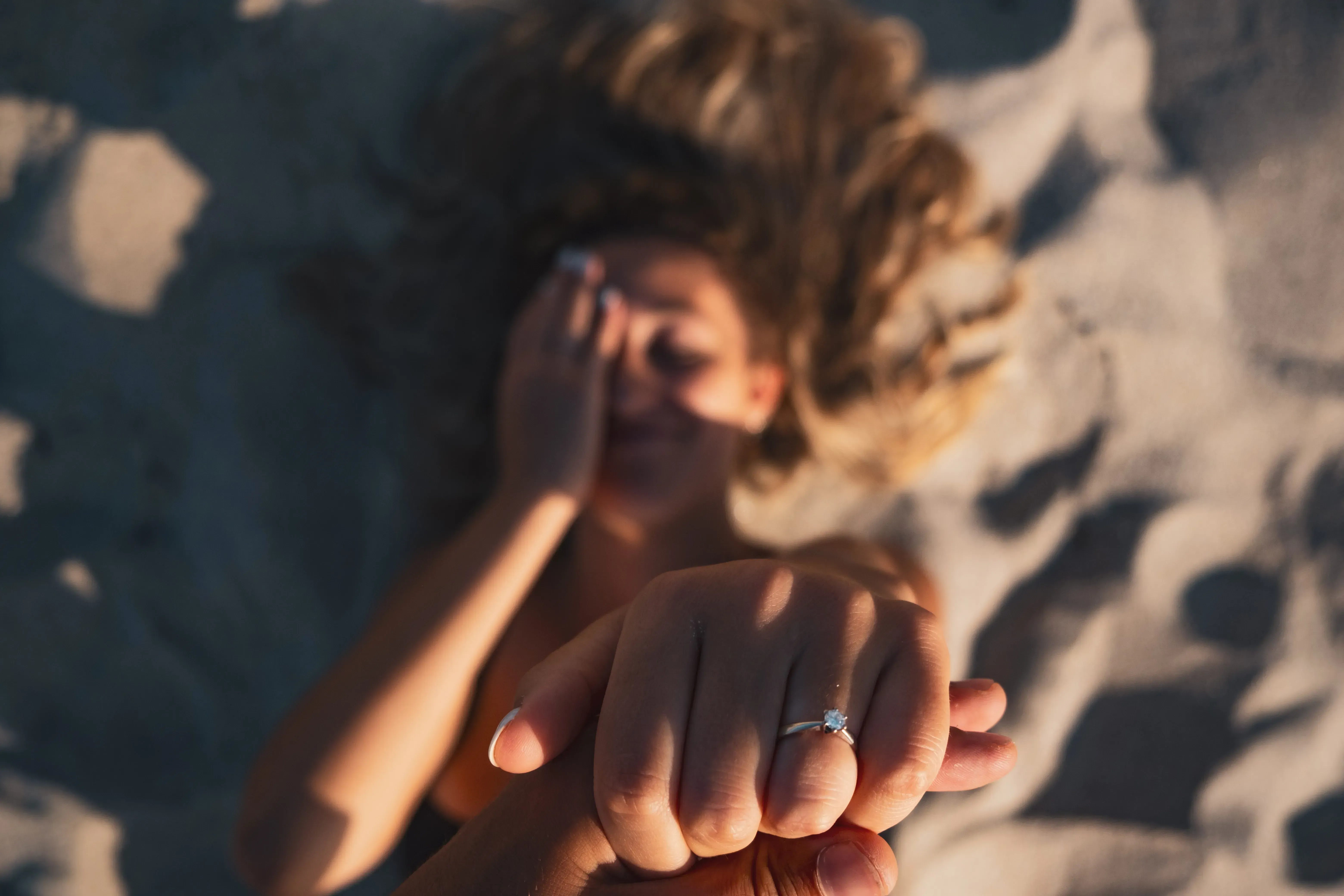 -up of Letizia's hand, showing a ring, resting on the bright beach sand while lying down
