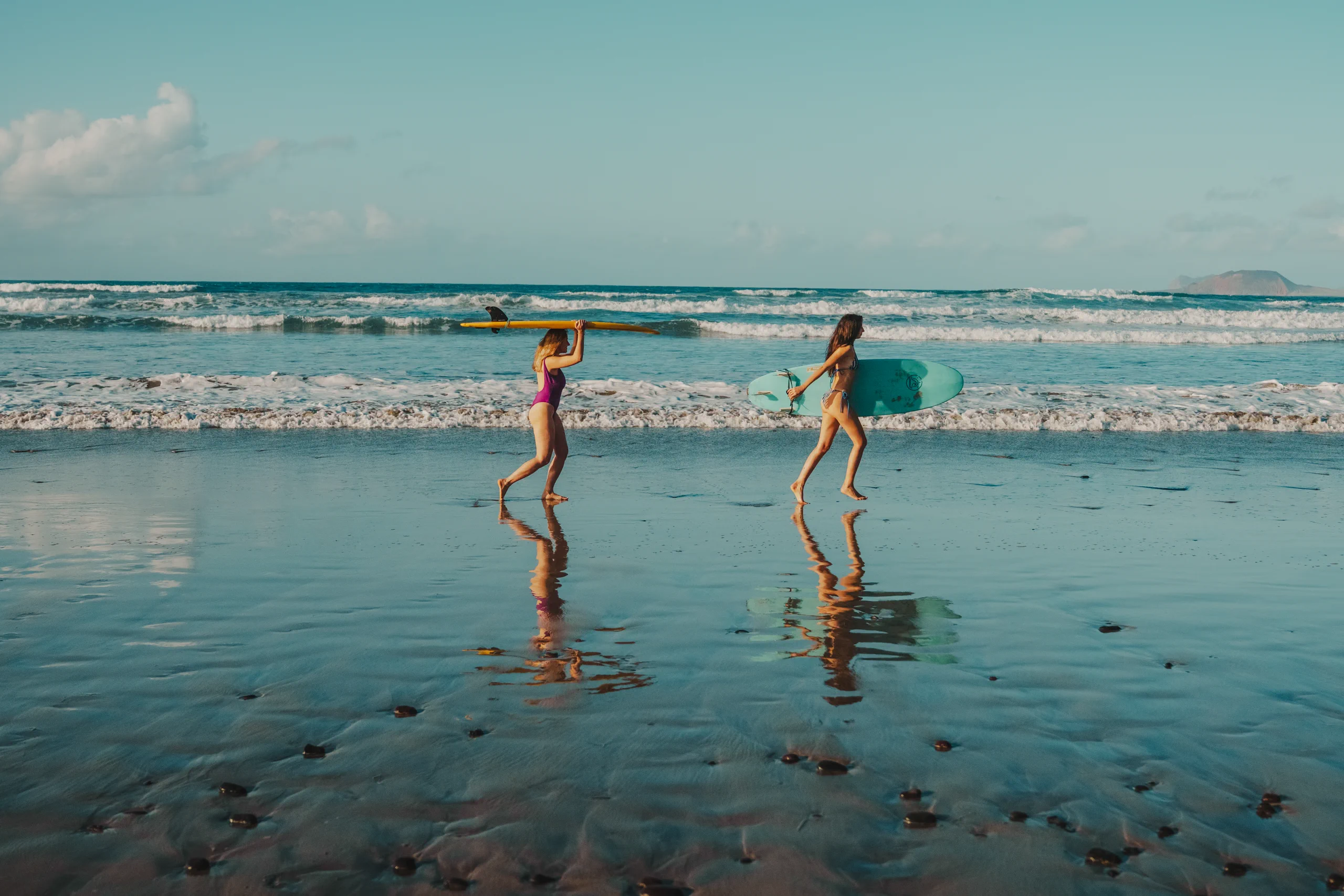 Letizia and miriam running on the beach with surf boards