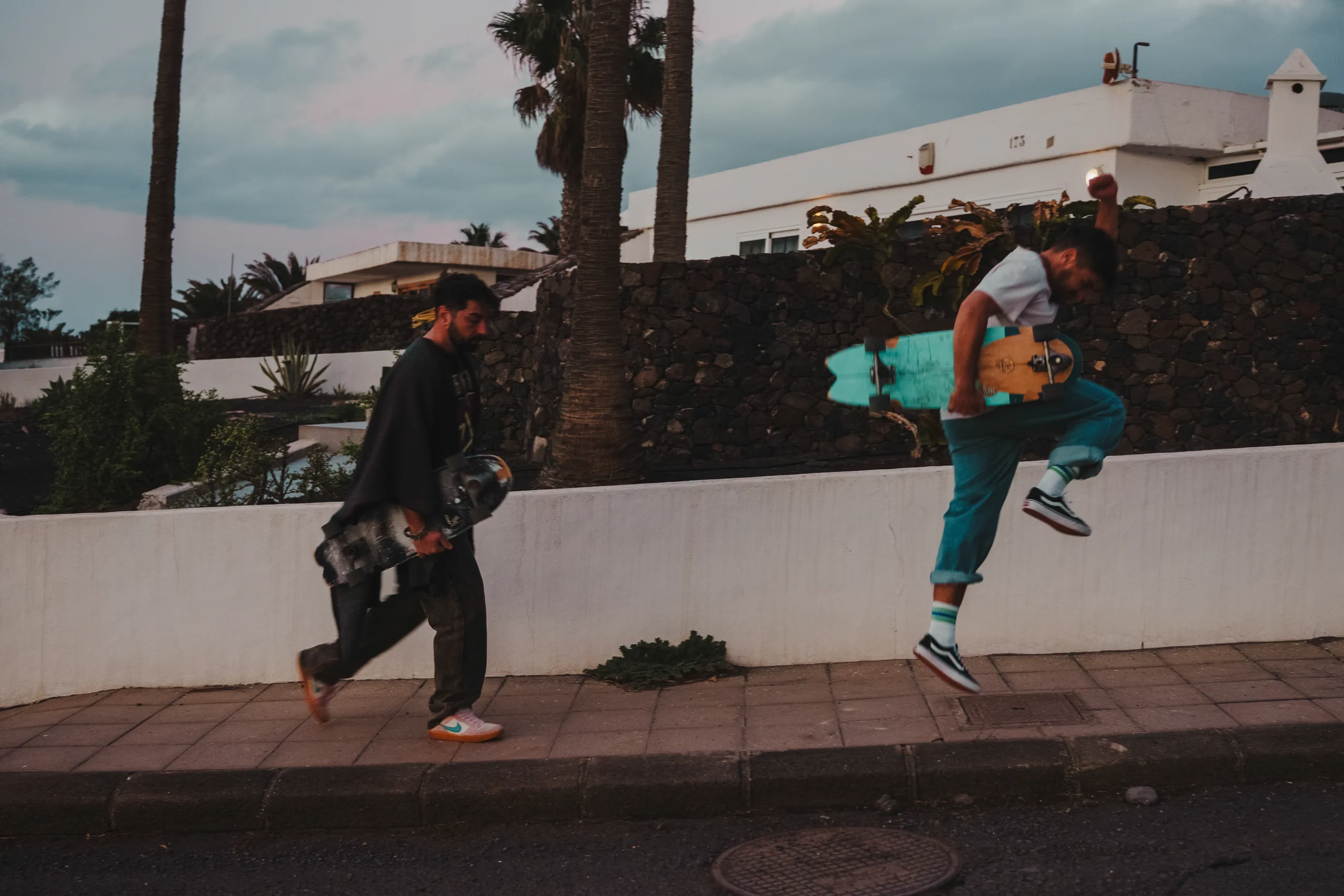Iair and Ieser walking up a road with two skateboard, while jumping
